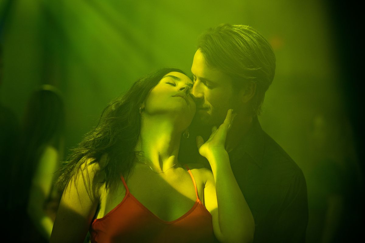 Glen Powell and Adria Arjona dancing in a green-lit club, getting steamy and almost kissing
