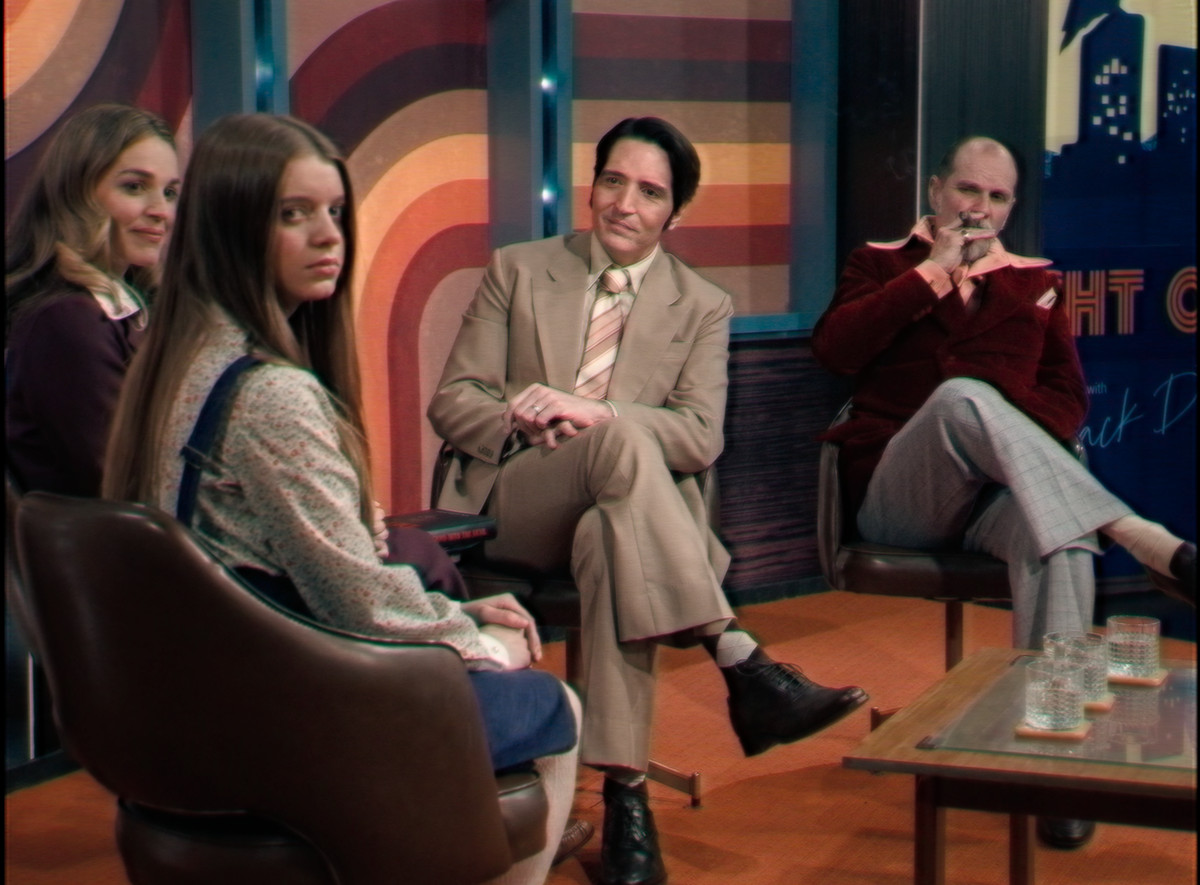Several people sit in a circle on a late night talk show set in Late Night with the Devil including David Dastmalchian, Ingrid Torelli, and Ian Bliss