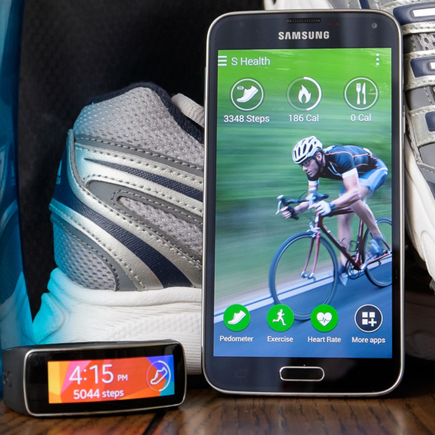A Samsung smart phone and a step counter placed near a pair of sneakers and a water bottle.