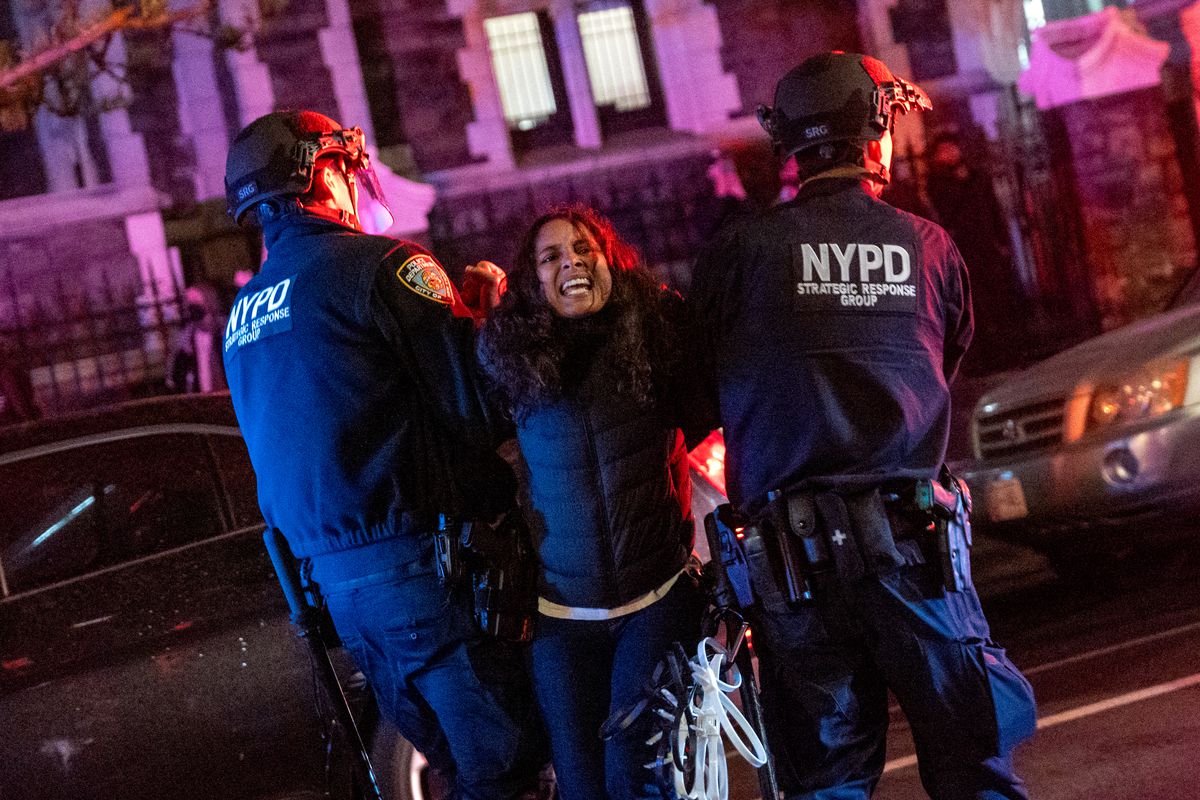Two NYPD officers hold the arm of a struggling protester as they walk down a city street.
