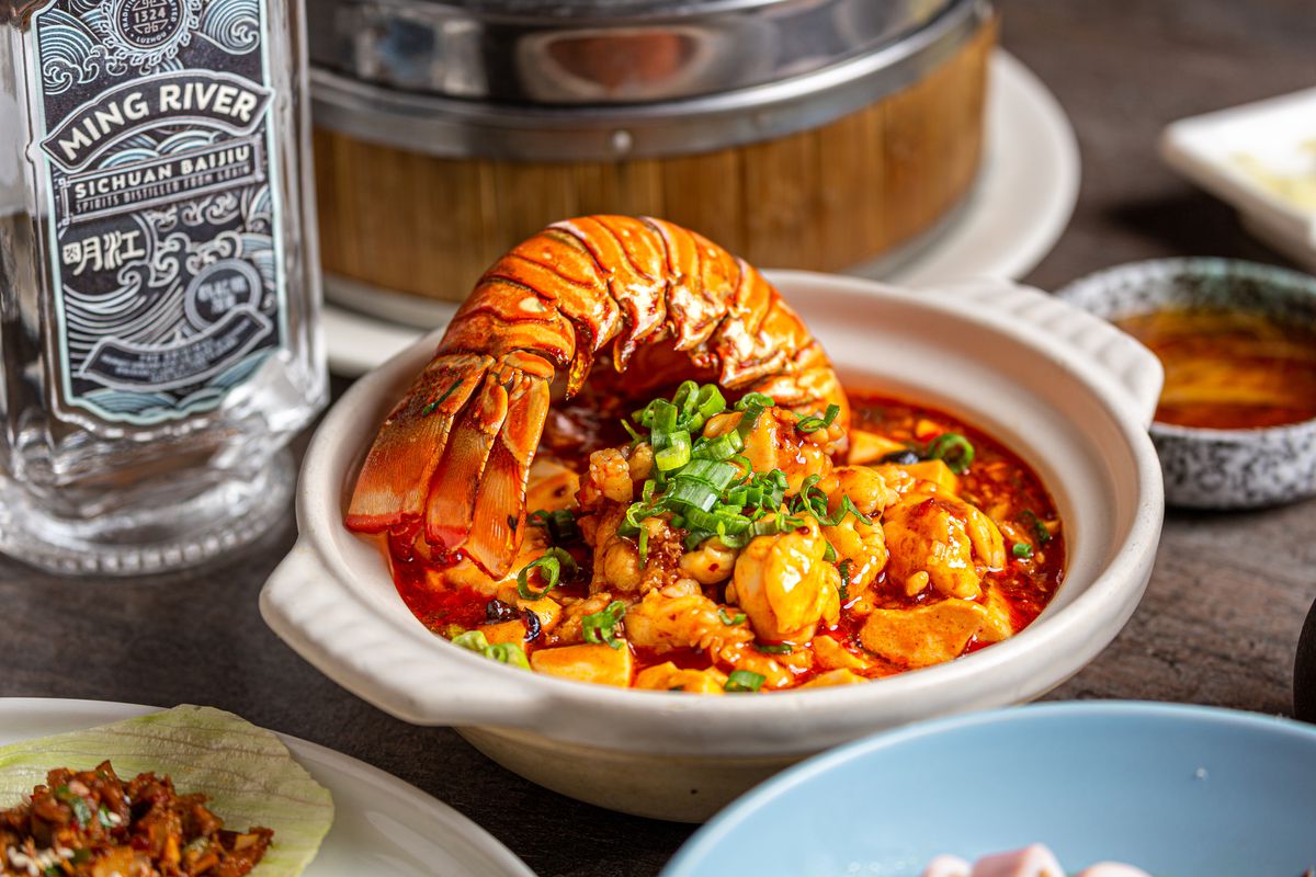 An image of lobster on top of a mapo tofu dish with a red sauce. A bottle of Asian liquor is next to the dish.