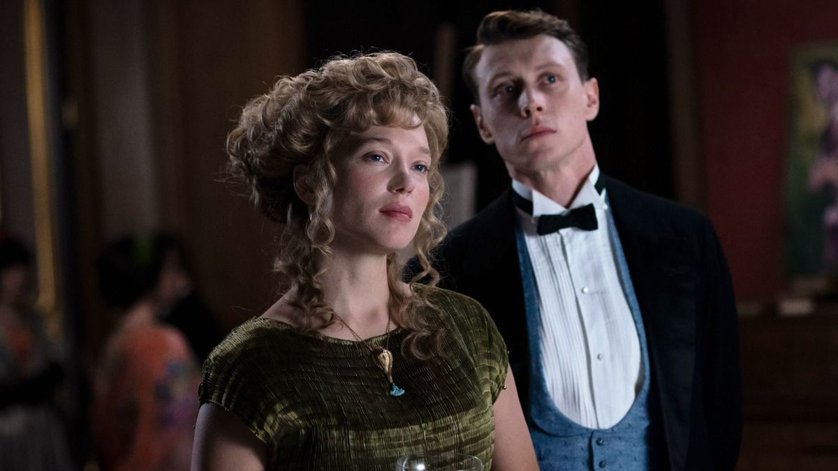 Gabrielle (Léa Seydoux) and Louis (George MacKay), a pale man and woman dressed in 1910 Parisian fashions —&nbsp;her in a green gown with her hair in ringlets, him in a black bow tie and jacket and blue vest —&nbsp;stand together, looking offscreen in a disaffected way in The Beast