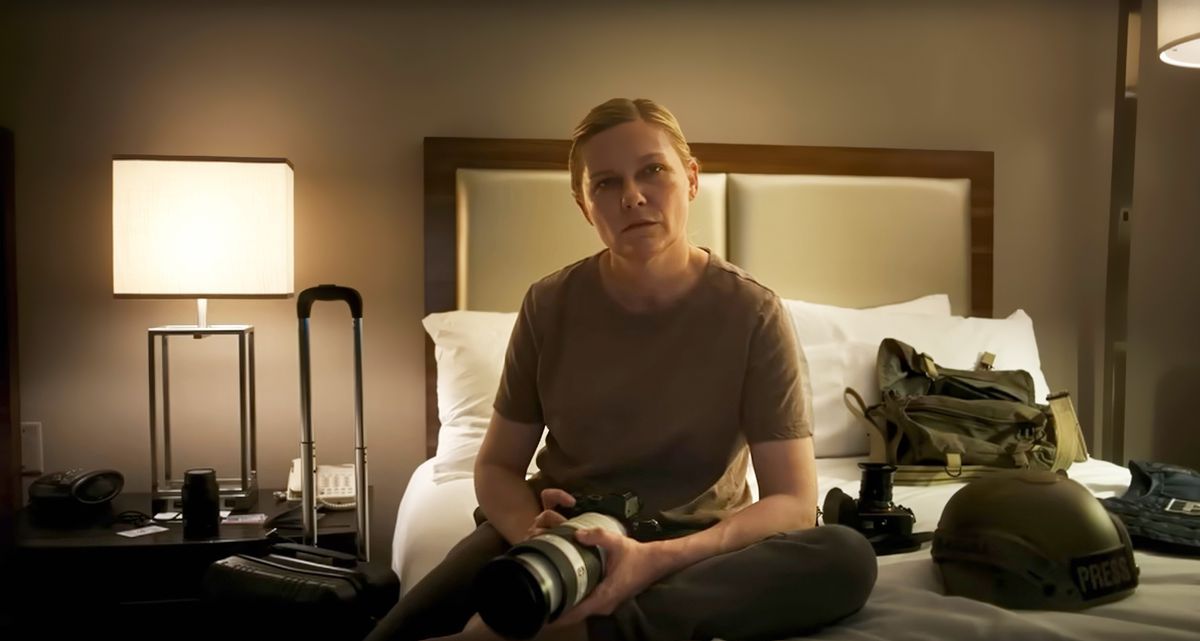 Photojournalist Lee (Kirsten Dunst) sits on a hotel-room bed and stares directly into the camera in Alex Garland’s Civil War