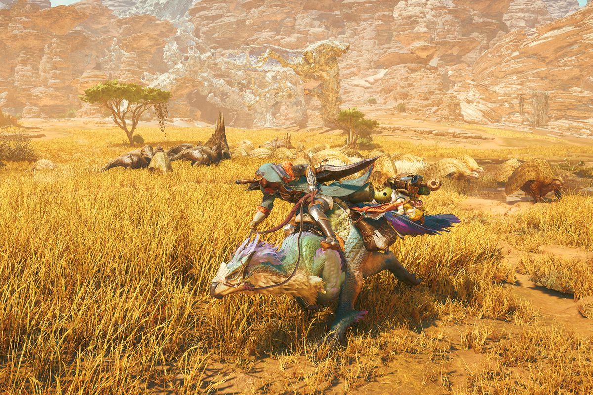 A hunter rides its steed, known as a Seikret, past a herd of dinosaur-like beasts roaming a desert plain in a screenshot from Monster Hunter Wilds