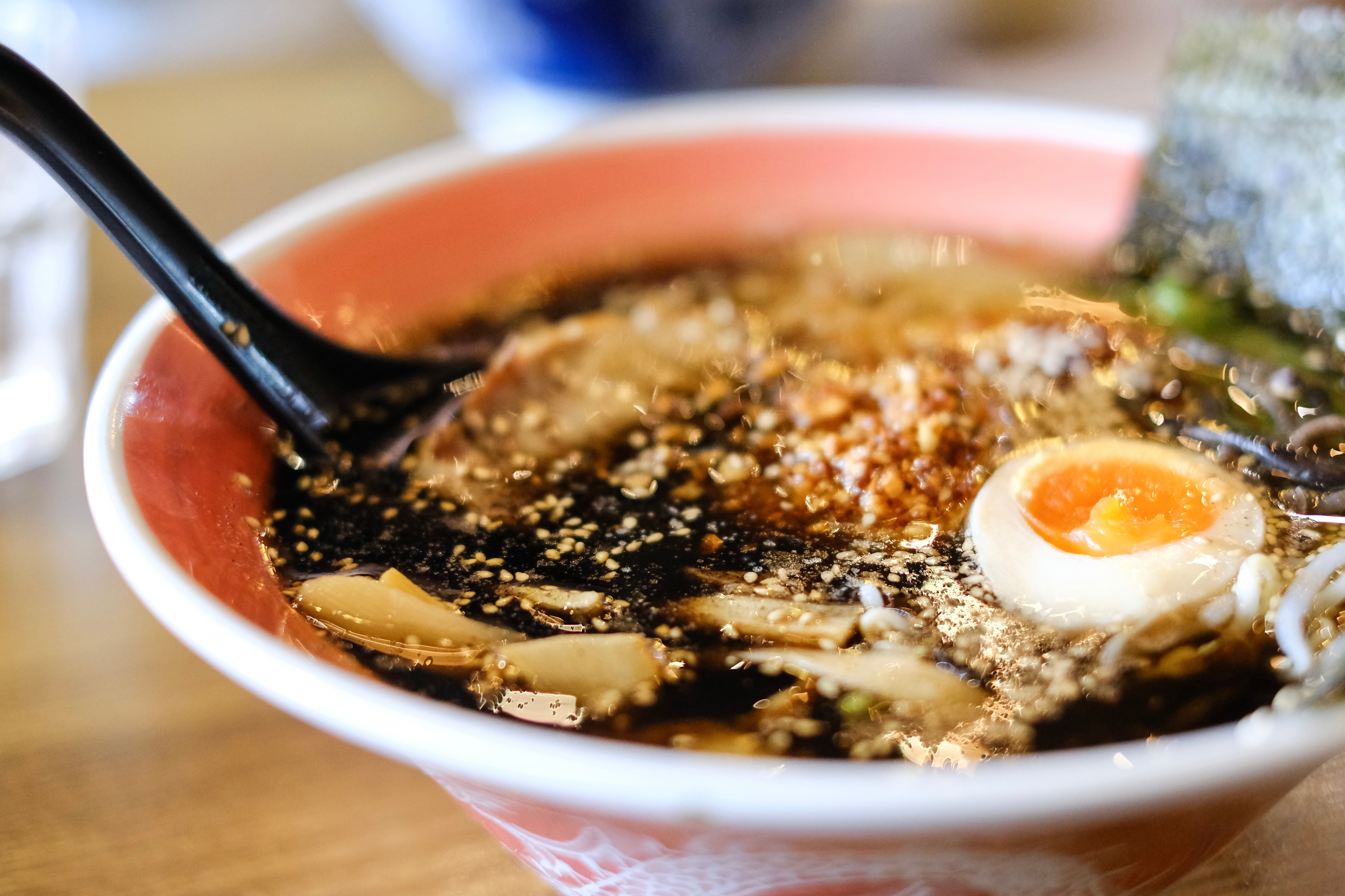 A red bowl of dark, rich tonkotsu ramen swimming with noodles and a halved hard-boiled egg on a wooden table. 