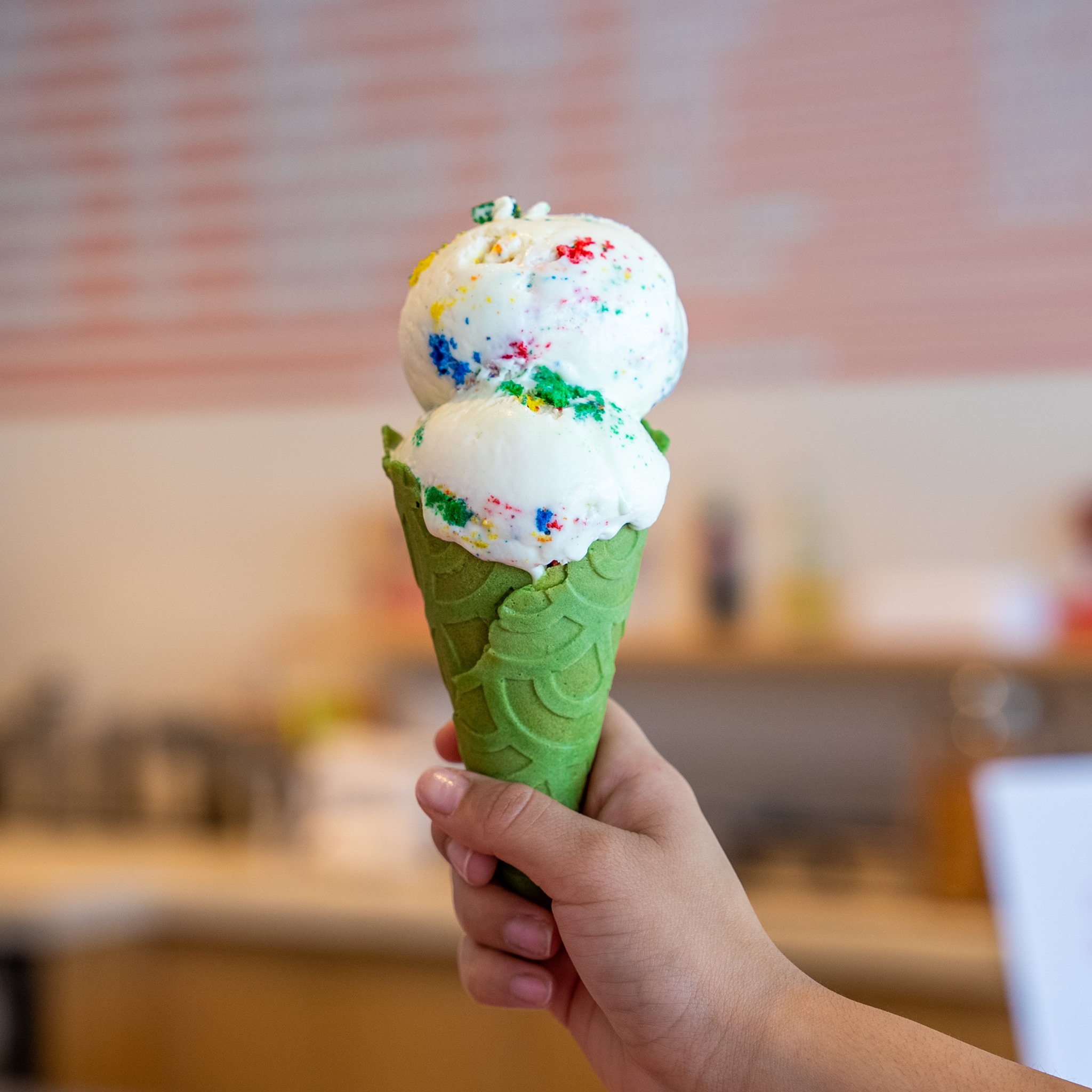An image of ice cream with multicolored pieces of cake, and a green matcha cone.