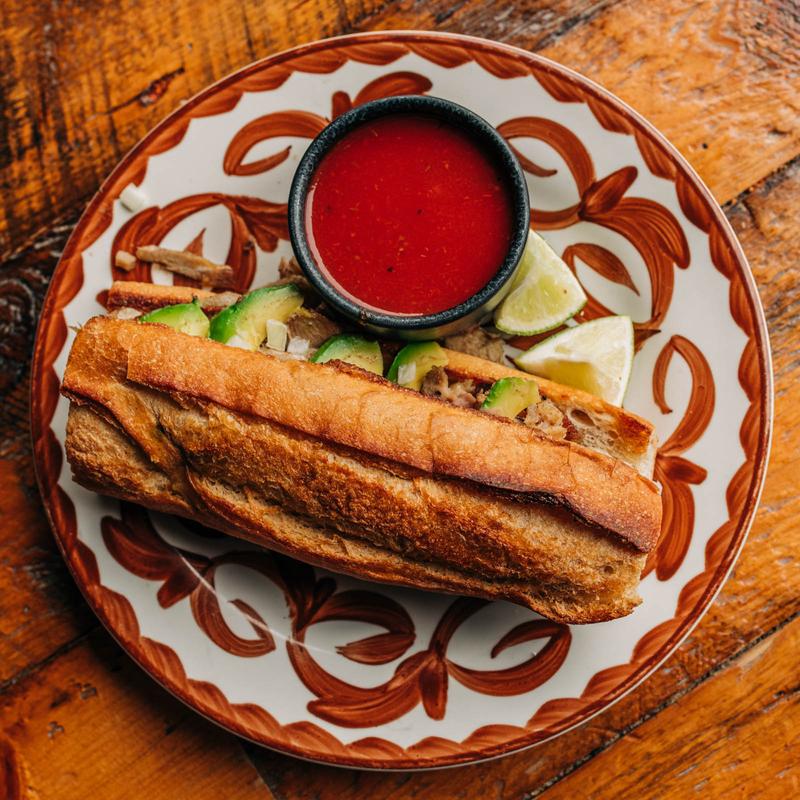 A long torta on a red and white patterend plate with a side of red salsa. 
