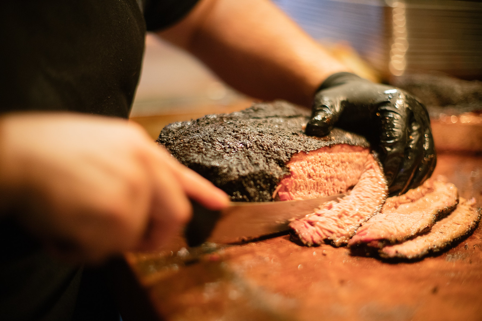 A chef holds down a slab of brisket and slices it into thin pieces.