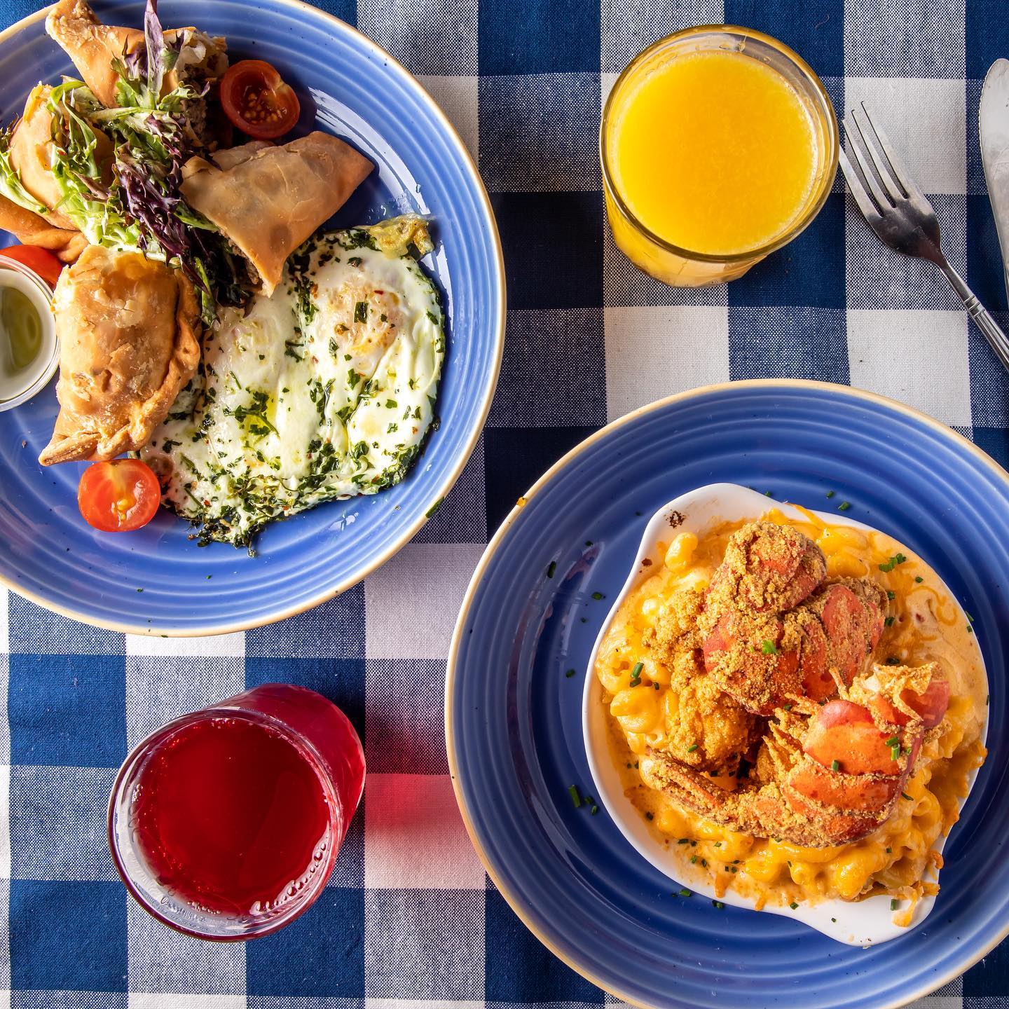 Two plates with brunch dishes on a checkered tablecloth, and two juice drinks on the side.