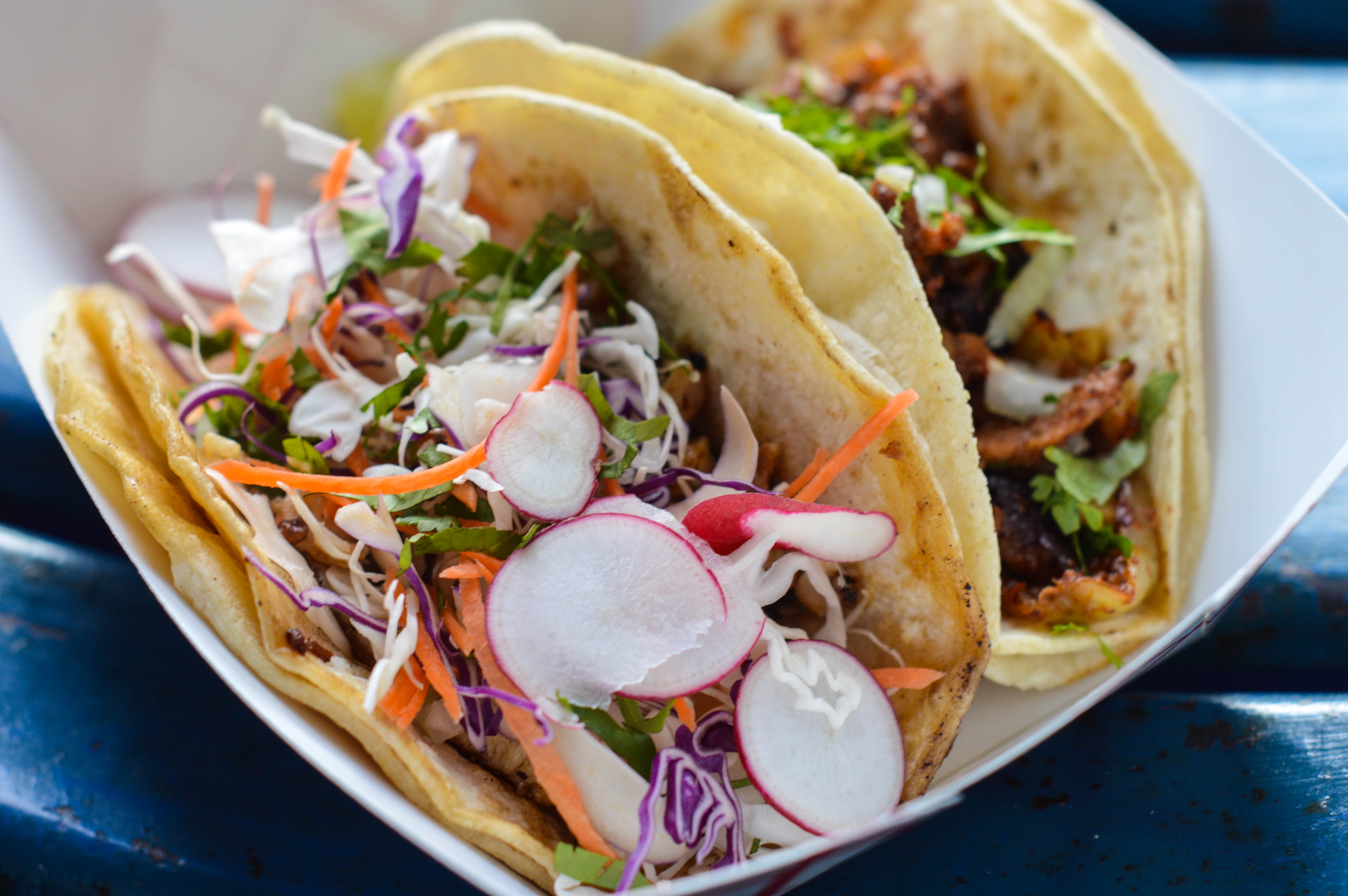 Two tacos loaded with meat and fresh veggies in a to-go basket.