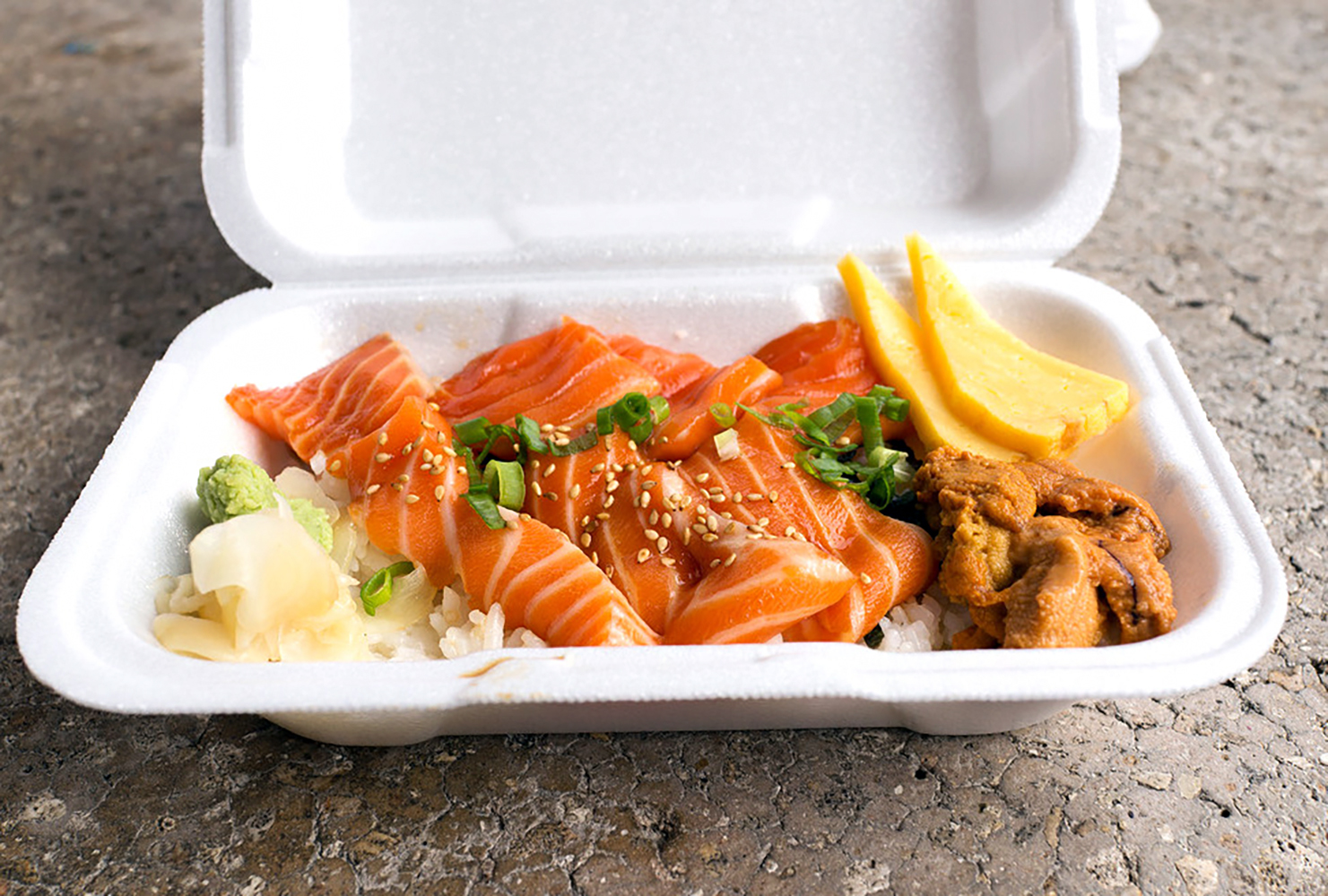 A takeout container full of slices of sashimi.