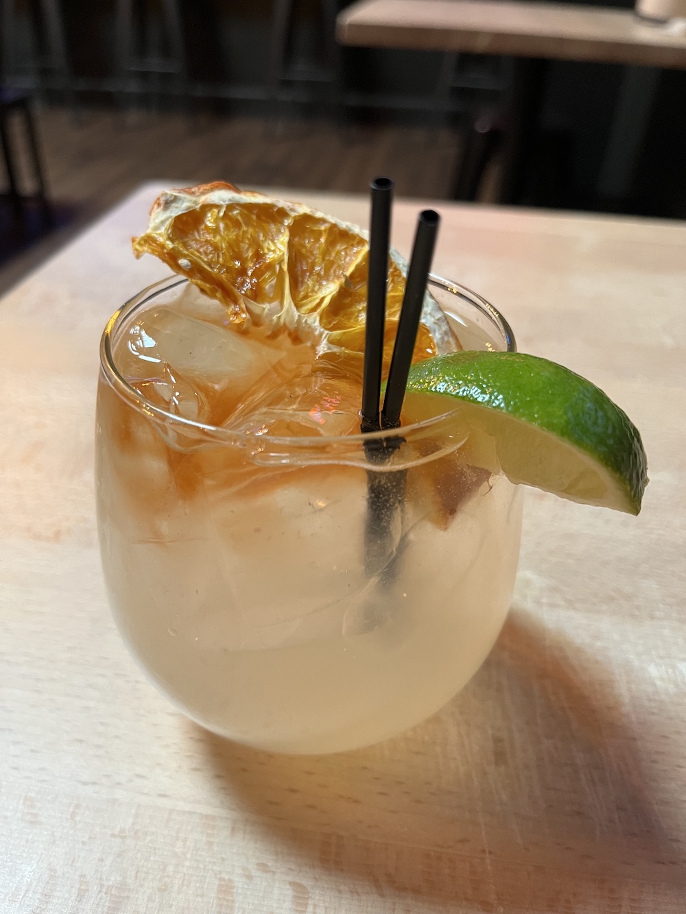 A cocktail with some sort of brown float, a dried orange slice and a lime wedge on the rim
