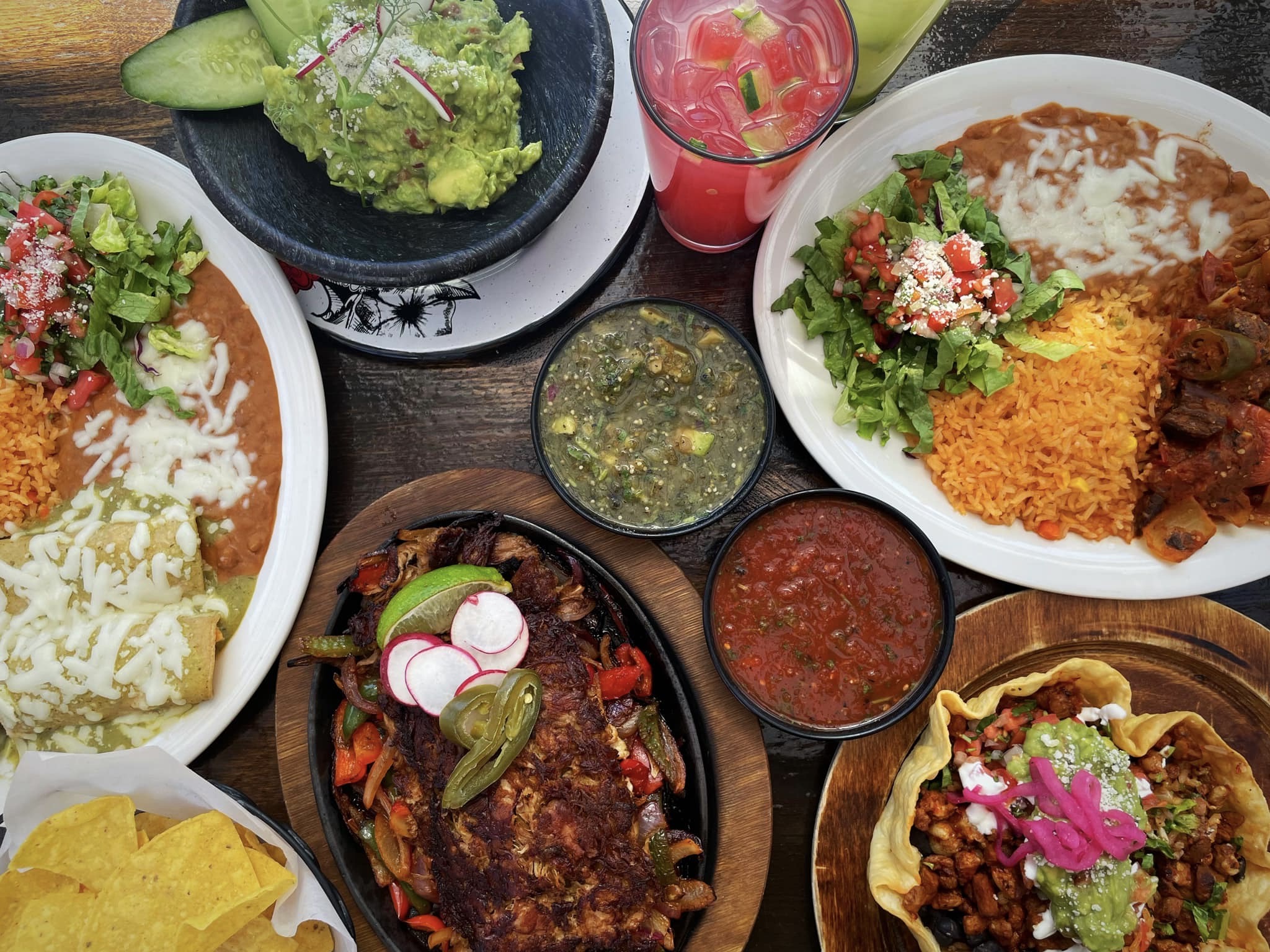 A spread of Mexican dishes like fajitas, enchiladas, and taco salads served with rice and beans and a pink margarita from Patria Cocina in Atlanta.
