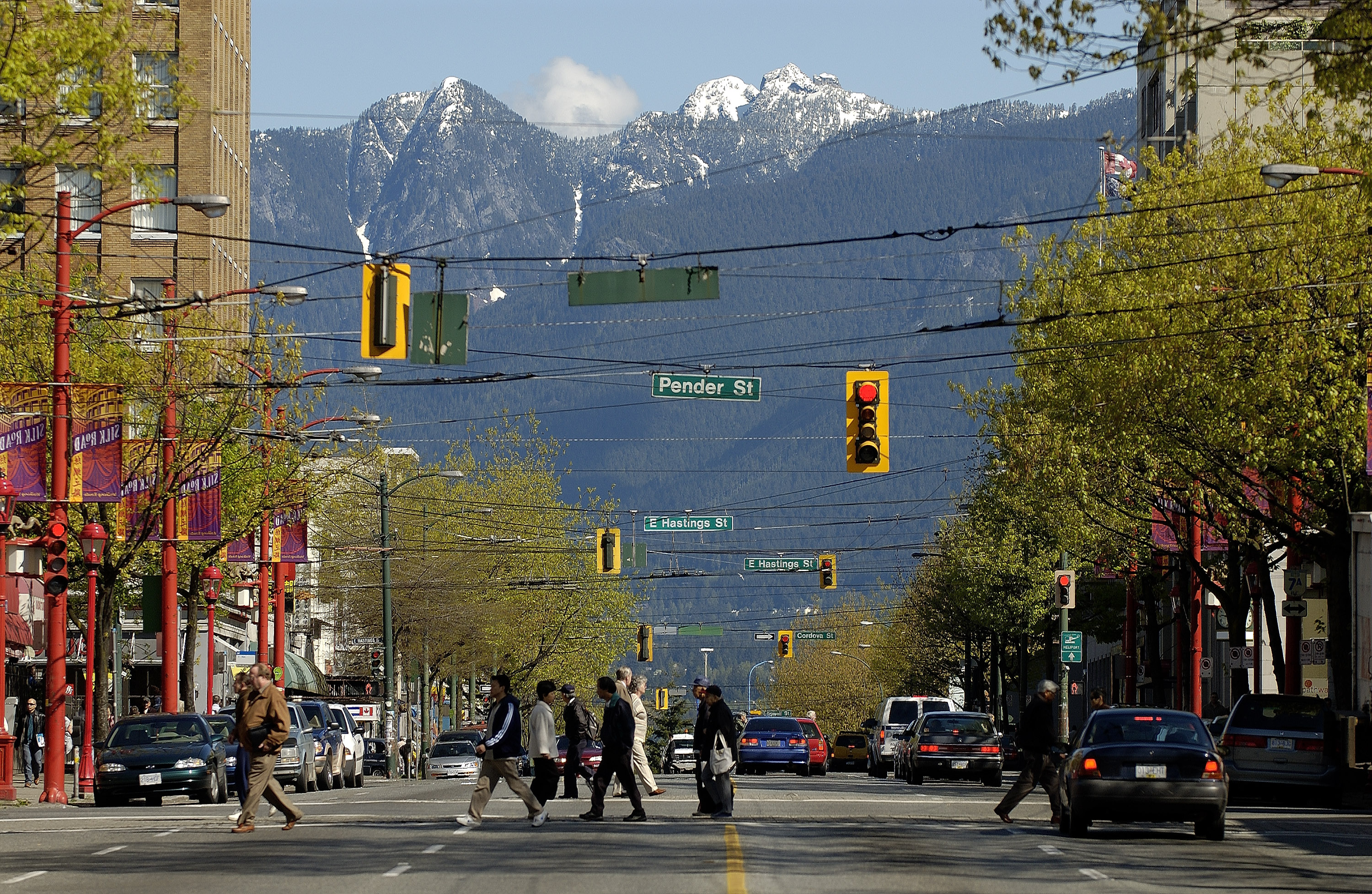 Residents cross a wide city street with snow-capped mountains filling the background.