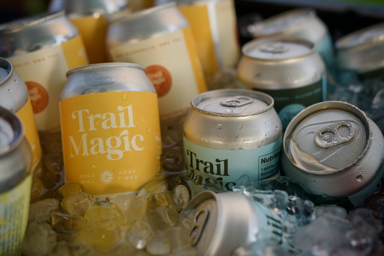 An assortment of aluminum cans with yellow and blue labels that read “trail magic” floating in ice water. 