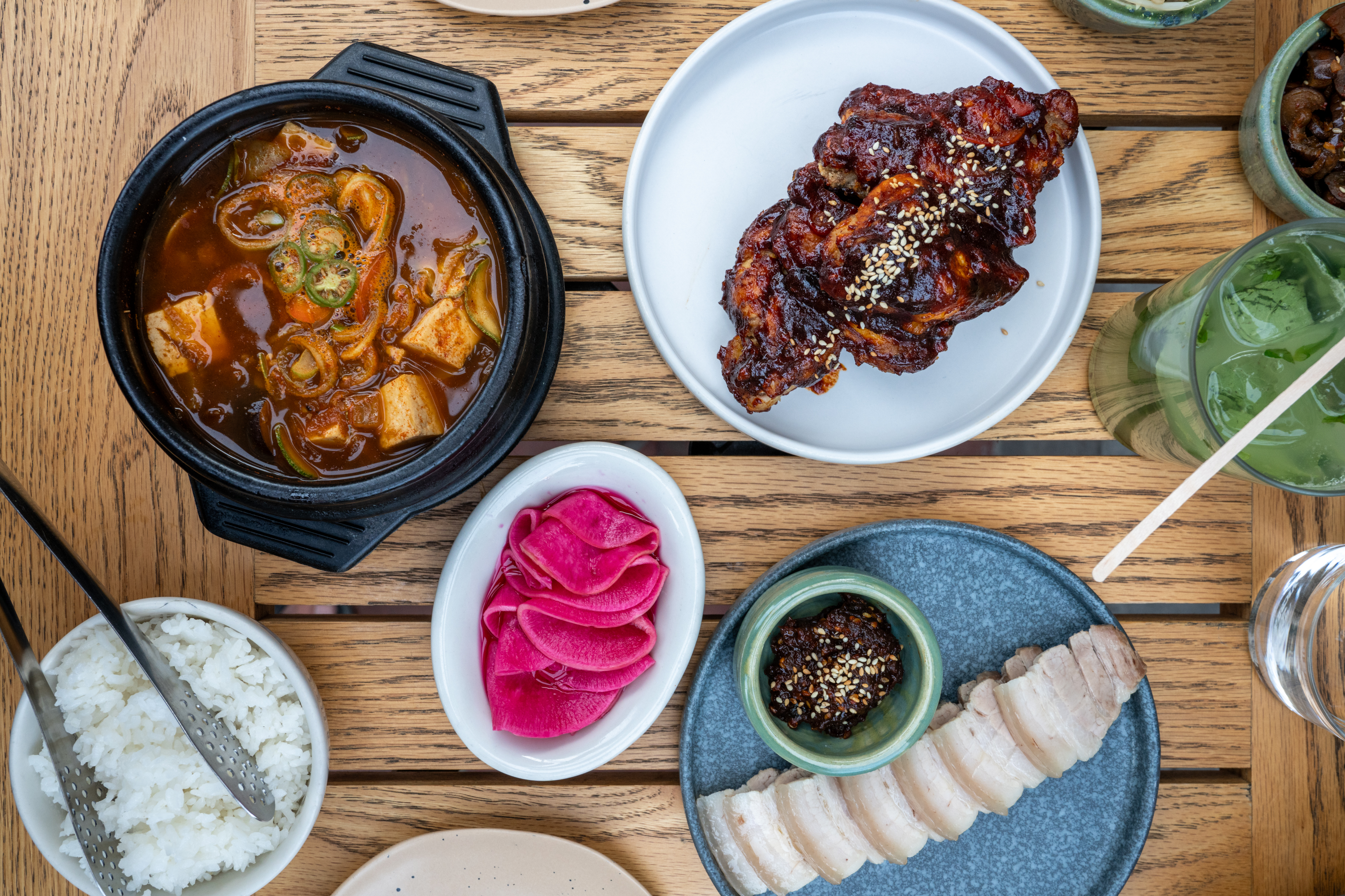 From above, a table laid with a spicy stew, glazed meat, pickled radishes, and other dishes.