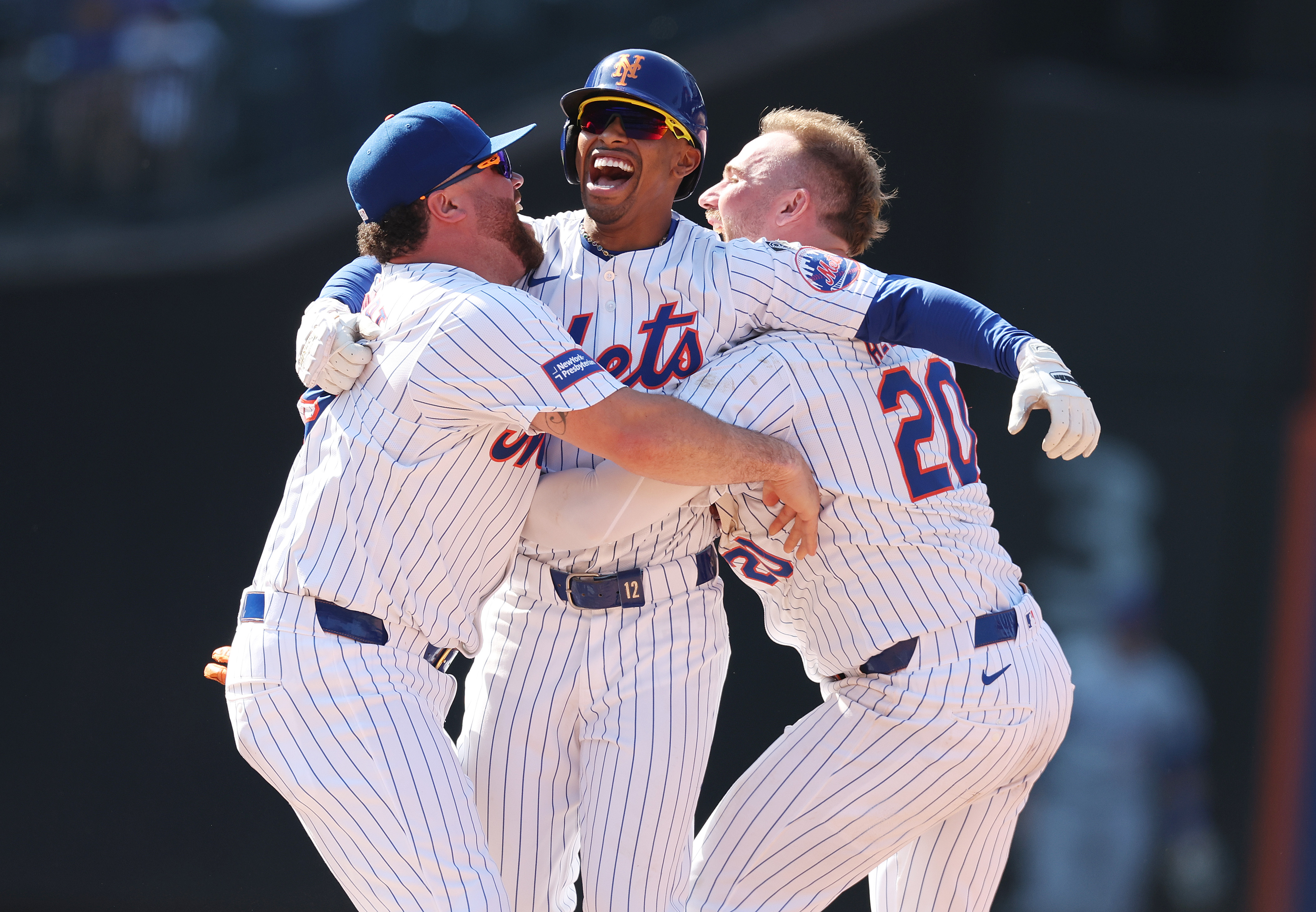 Francisco Lindor celebrating with DJ Stewart and Pete Alonso, all of whom are in white Mets jerseys with blue lettering and blue pinstripes.