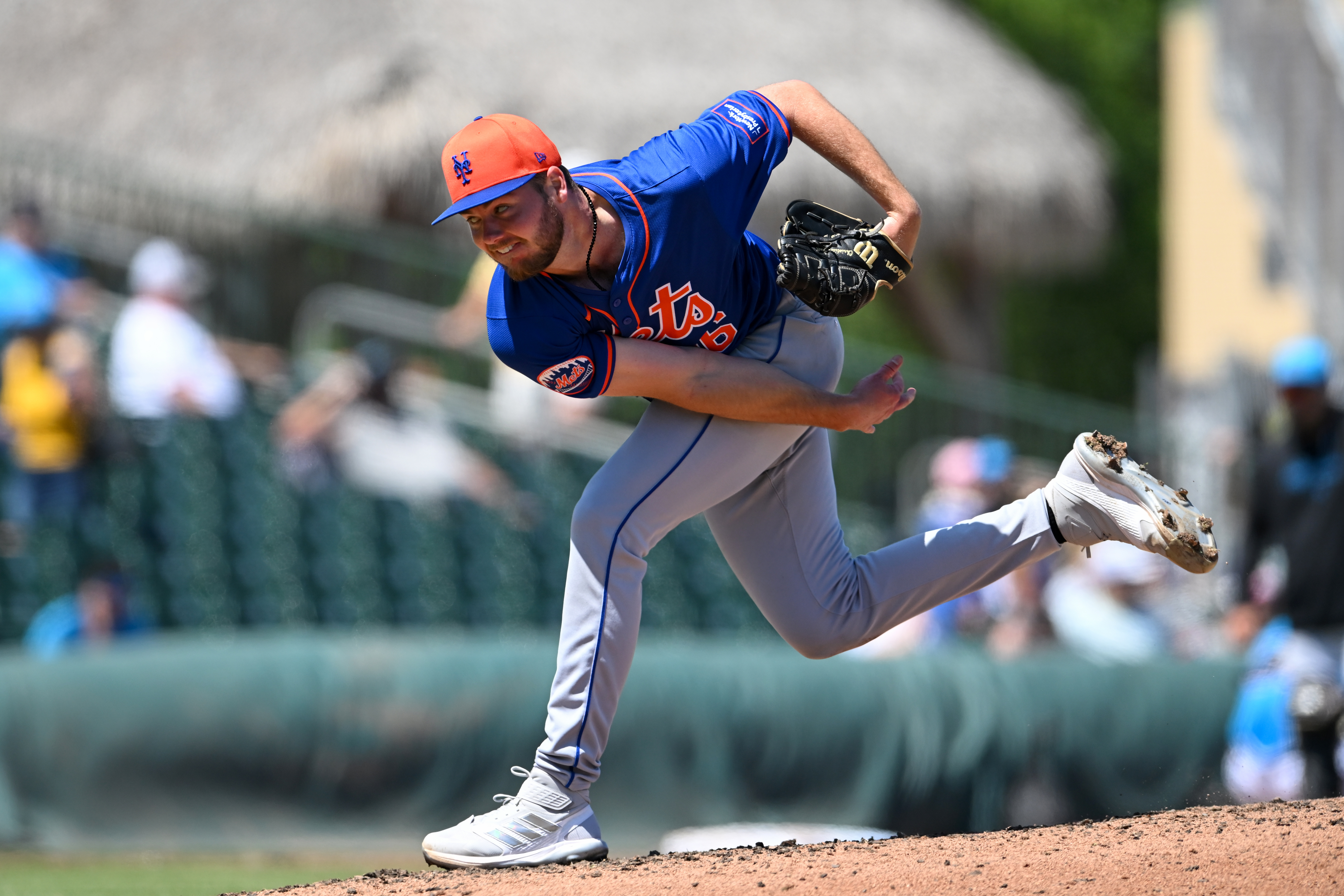 Christian Scott throws a pitch in a blue Mets jersey with an orange and blue hat.