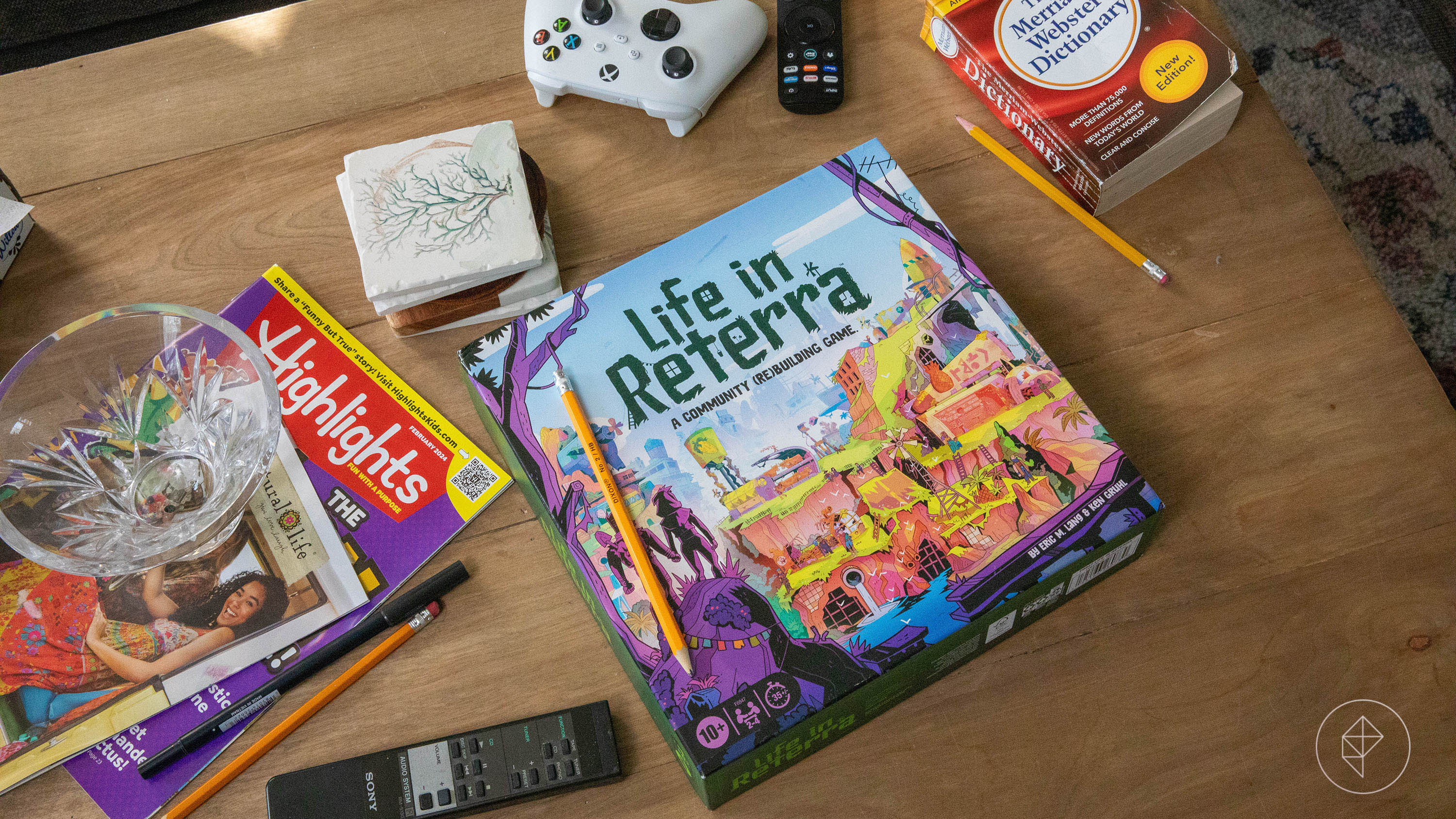 The game box for Life in Reterra on a coffee table filled with controllers, magazines, catalogs, and other detritus of modern life.