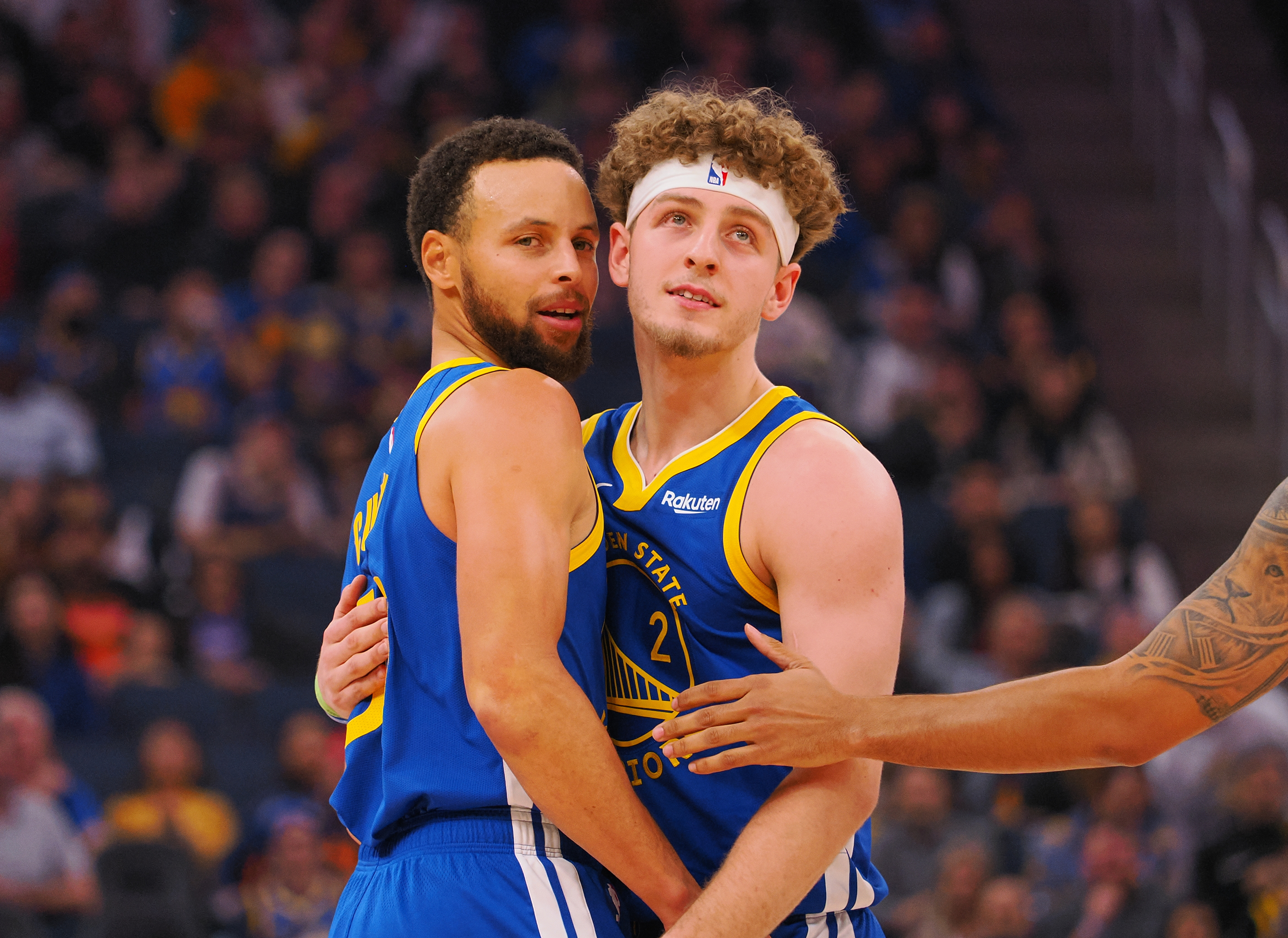 Steph curry and Brandin Podziemski, hugging while looking over their shoulders.