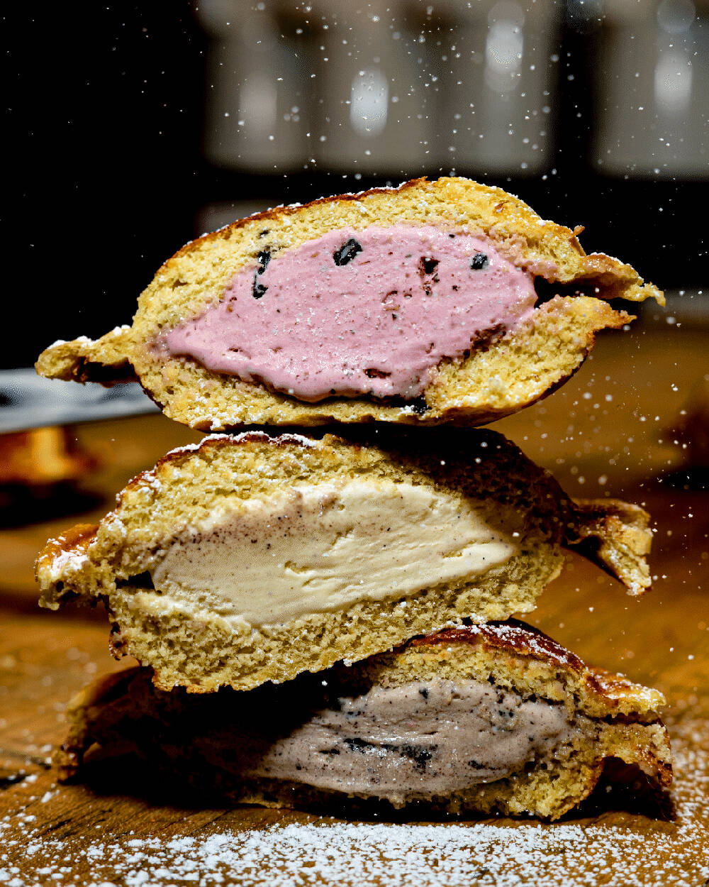 Three dolce caldo cut in half and stacked on top of one another; one with berry ice cream in the center, one with a caramel colored ice cream, and one with a chocolate ice cream.