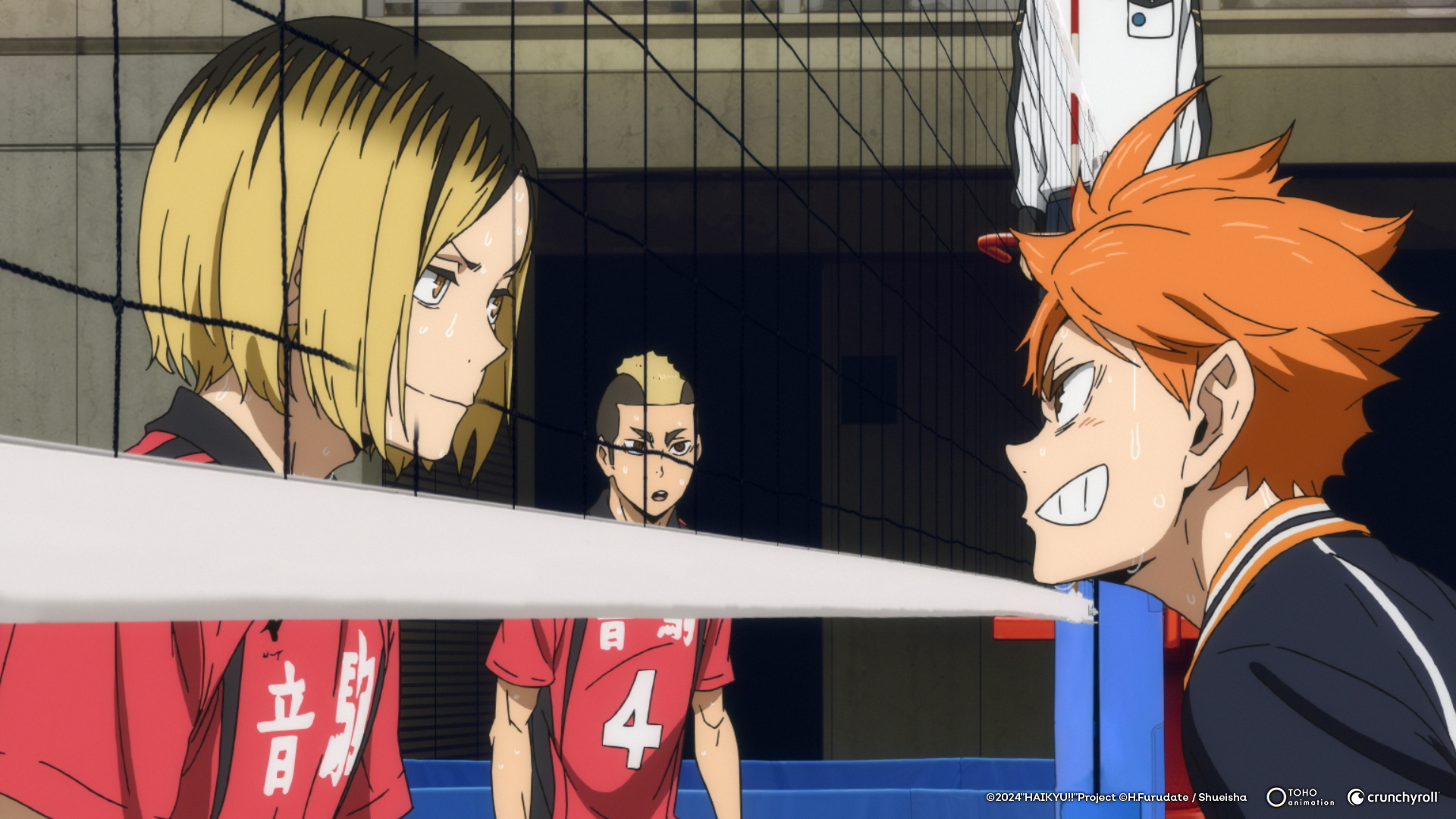 A blond boy in a red uniform and an orange-haired boy in a black uniform face off through a volleyball net in Haikyu!! The Dumpster Battle