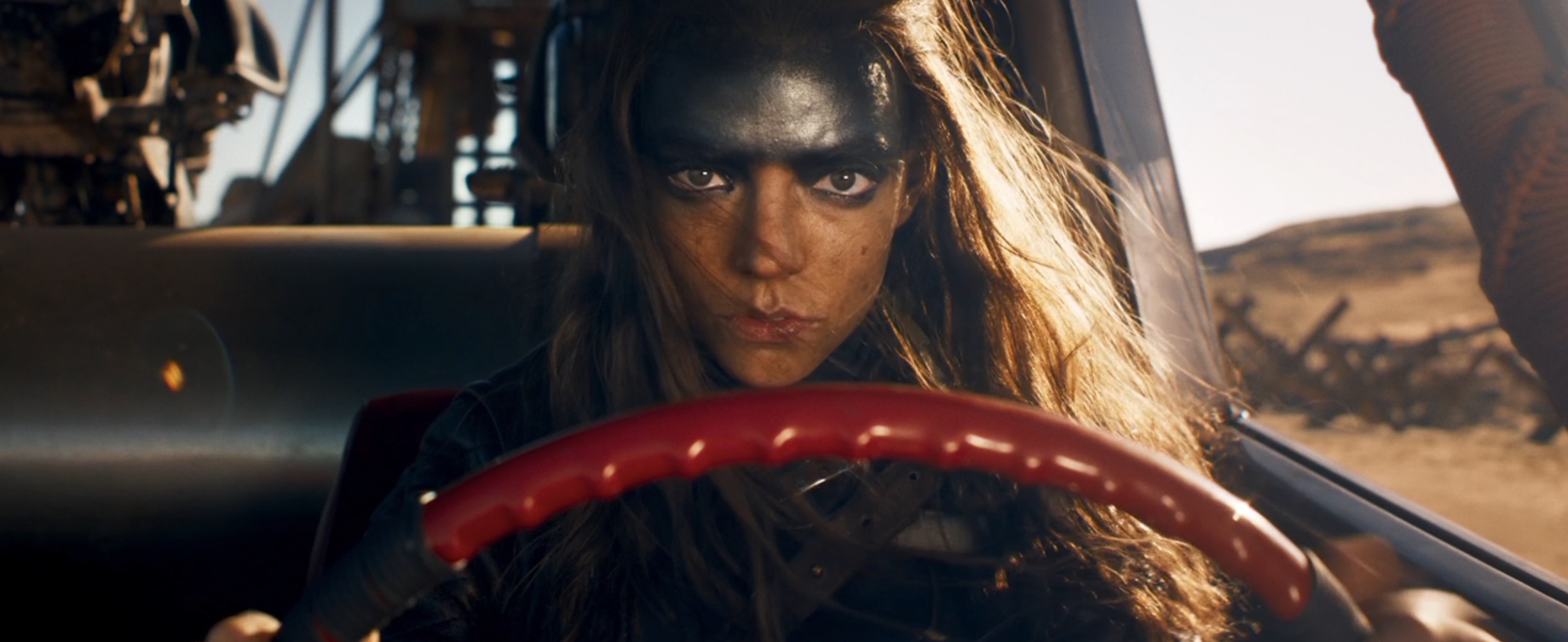 Furiosa (Anya Taylor-Joy), forehead smeared with greasepaint, drives the war rig in George Miller’s Furiosa
