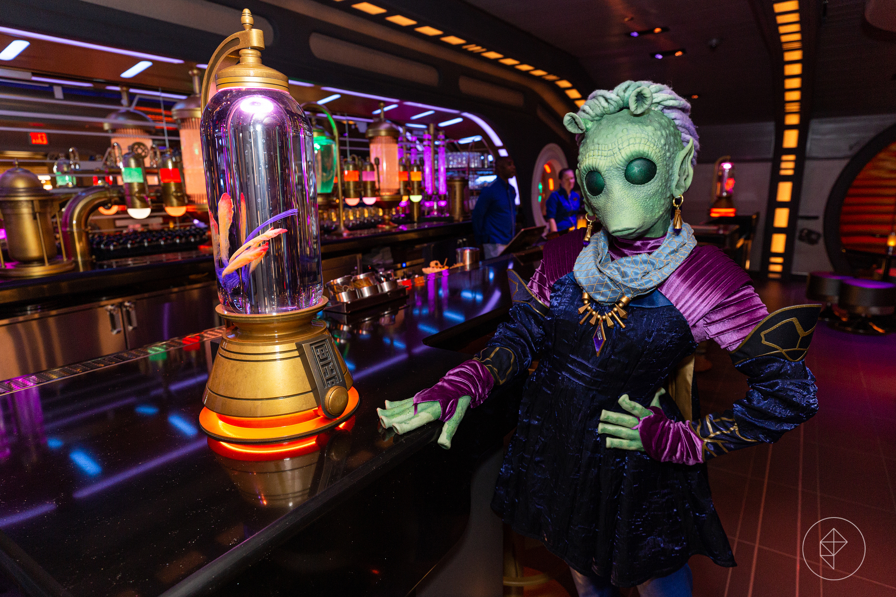 A woman in a green alien costume poses by a lavish bar, trimmed in gold and neon, in Disney’s Galactic Starcruiser