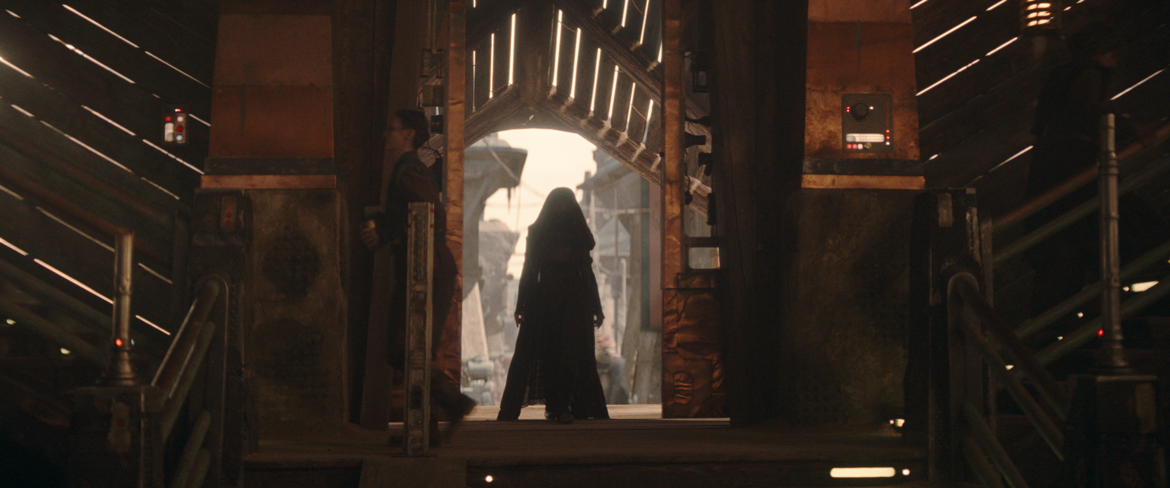 Mae (Amandla Stenberg) stands in a hood walking through a door way in Star Wars: The Acolyte