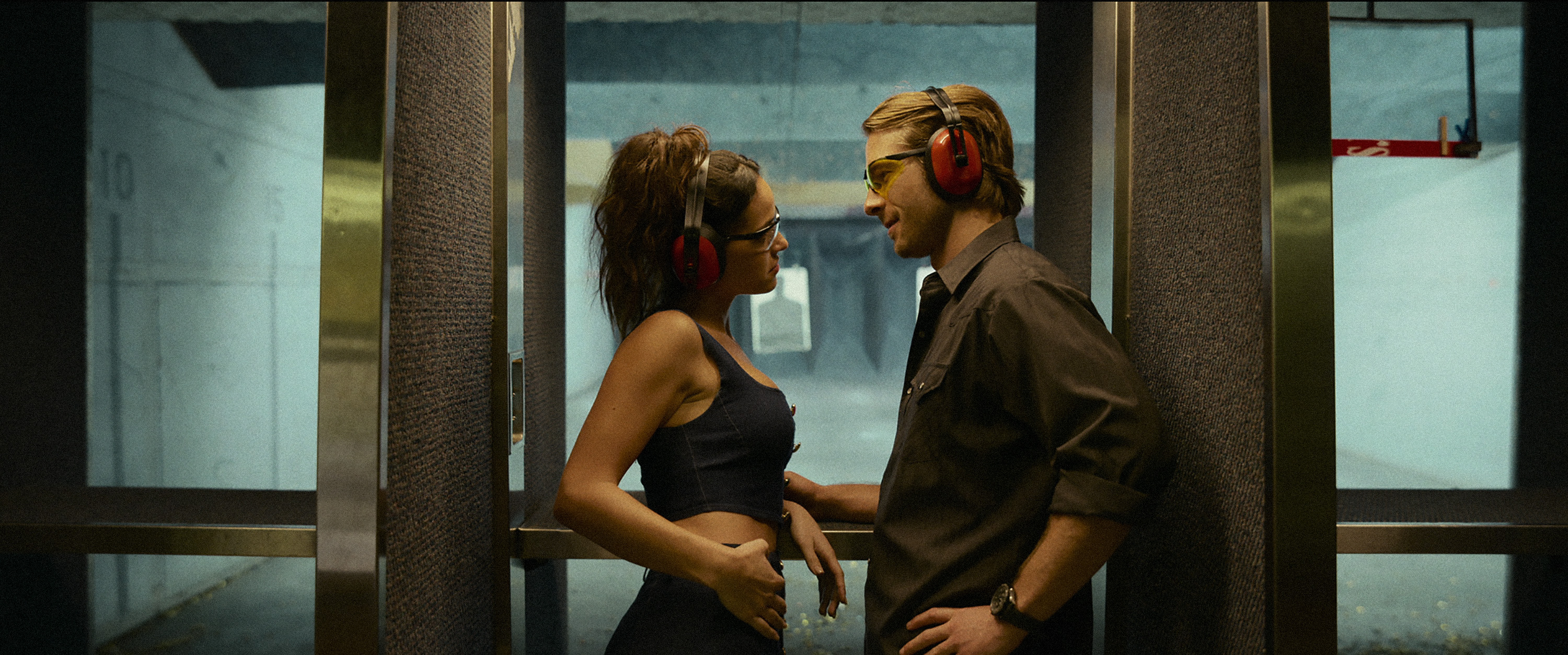 Adria Arjona and Glen Powell stare romantically into each other’s eyes at a firing range in Hit Man