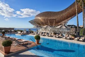 duży basen z krzesłami i dużym parasolem w obiekcie Hotel Arts Barcelona w Barcelonie