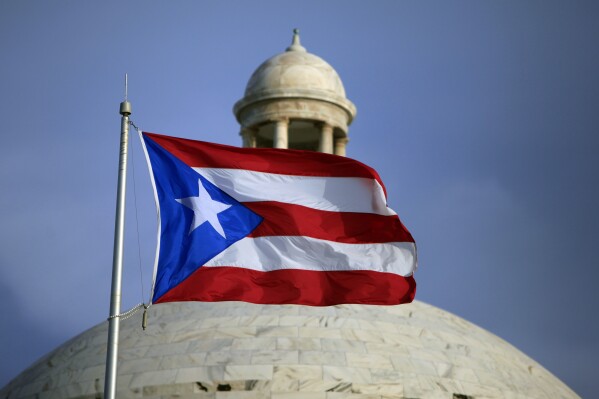 FILE - A Puerto Rican national flag flies in front of the Capitol building in San Juan, Puerto Rico, July 29, 2015. The island’s two biggest political parties hold gubernatorial primaries on Sunday, June 2, 2024. (AP Photo/Ricardo Arduengo, File)