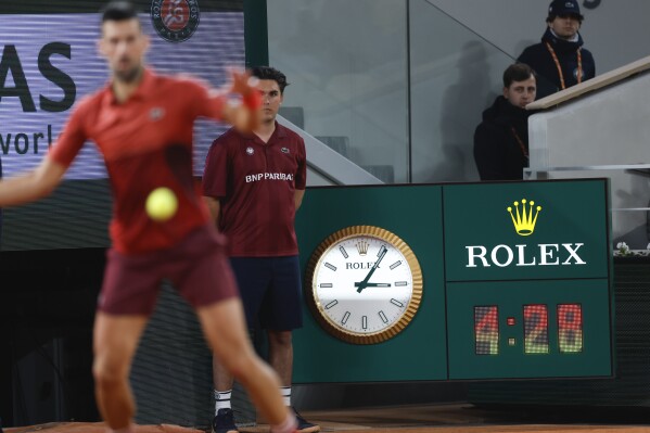 Serbia's Novak Djokovic plays a shot against Italy's Lorenzo Musetti as the clock indicates the match time played in the fifth set of their third round match of the French Open tennis tournament at the Roland Garros stadium in Paris, Sunday, June 2, 2024. (AP Photo/Jean-Francois Badias)