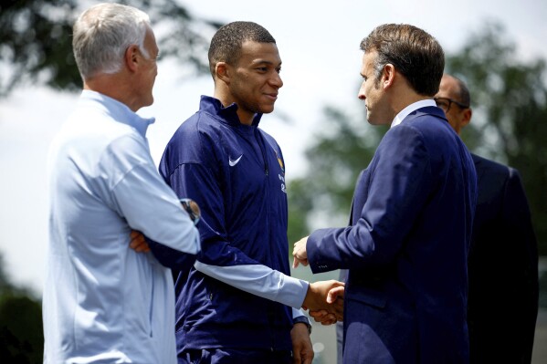 French President Emmanuel Macron, right, shakes hands with French soccer player Kylian Mbappe next to head coach Didier Deschamps as he arrives for lunch at the national soccer team training center in Clairefontaine, west of Paris, Monday, June 3, 2024 ahead of the UEFA Euro 2024. (Sarah Meyssonnier/Pool Photo via AP)