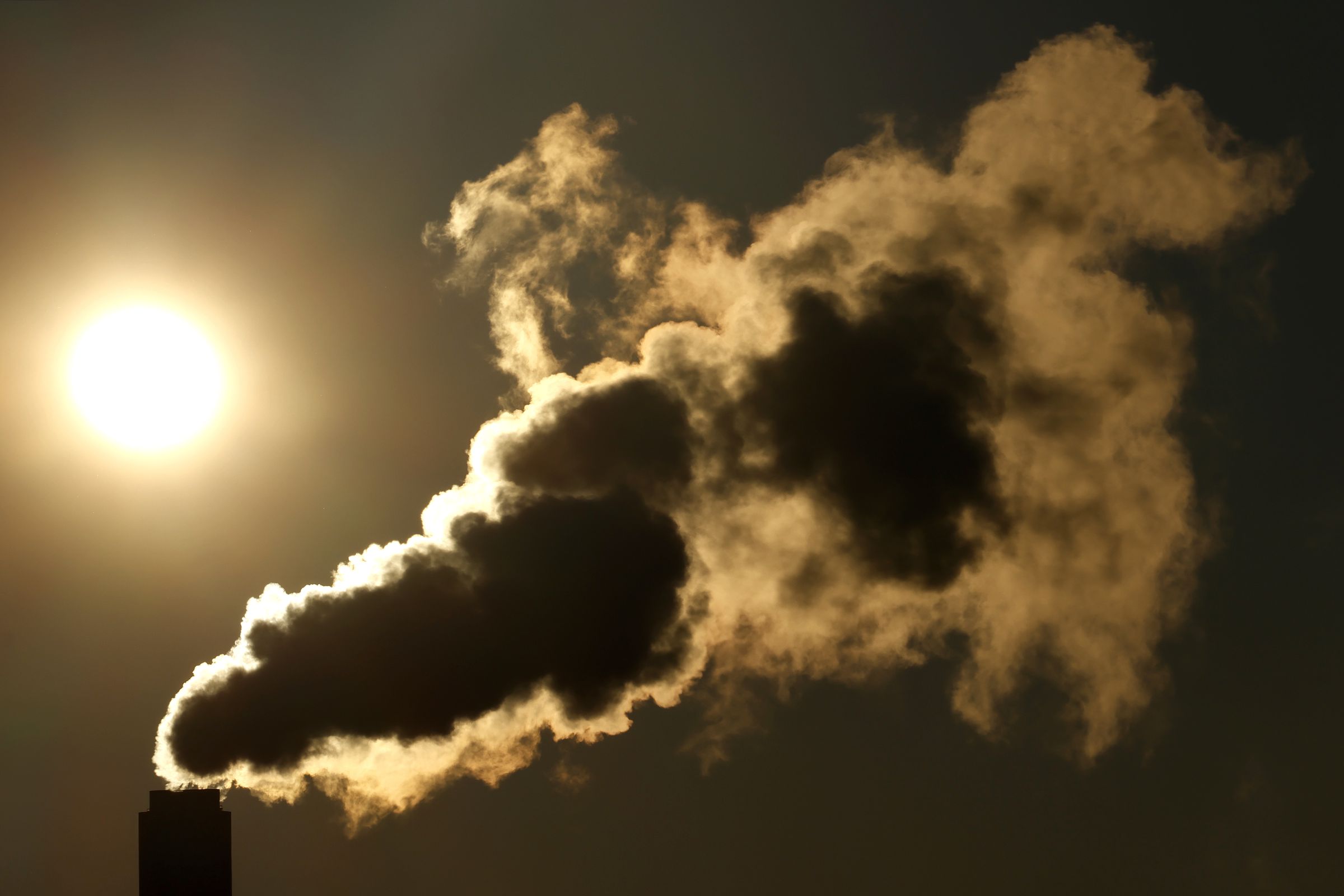 A plume of smoke rises from a smoke stack as the sun rises 