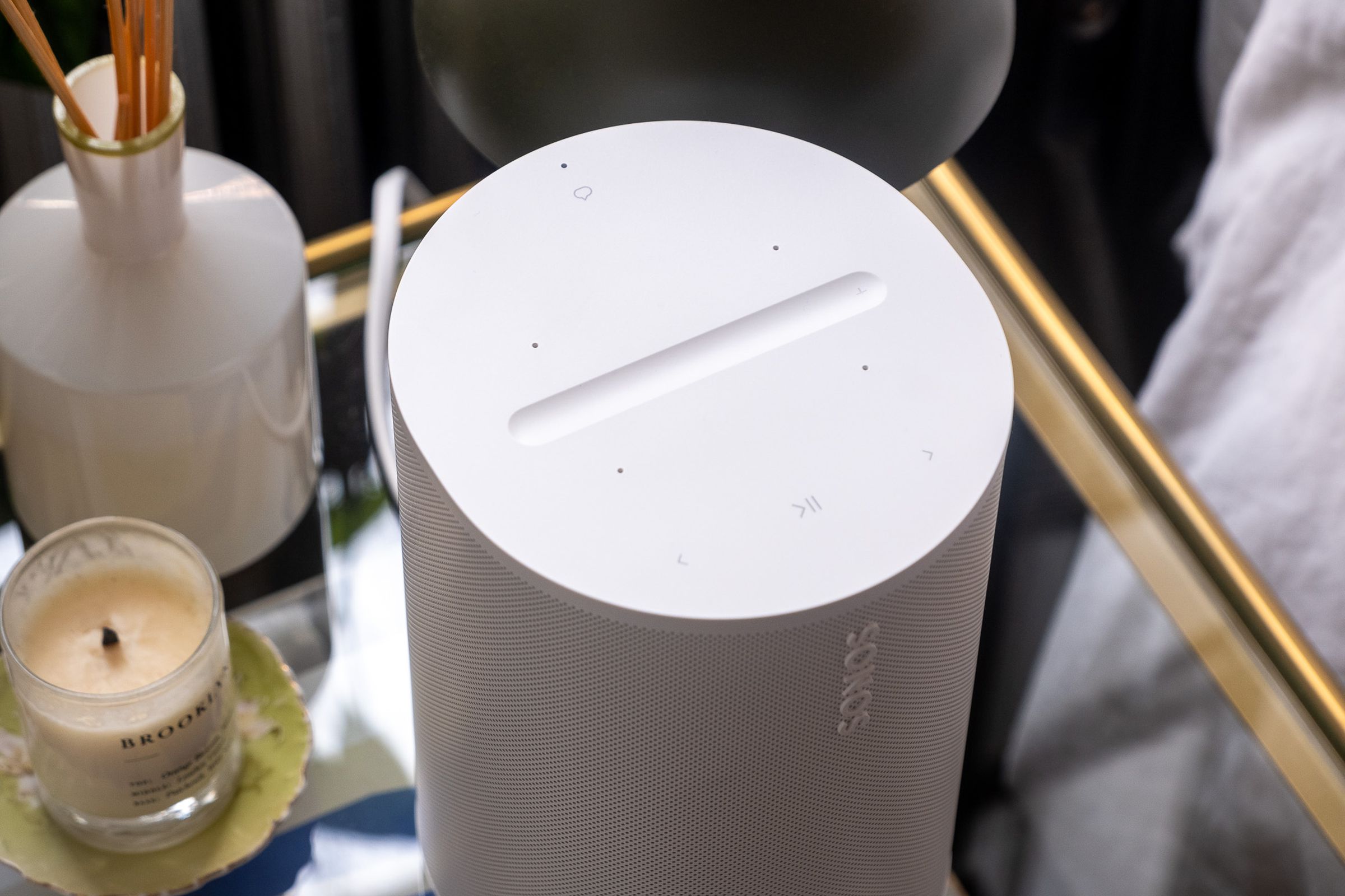 A photo of the Sonos Era 100 speaker on a bedside nightstand.