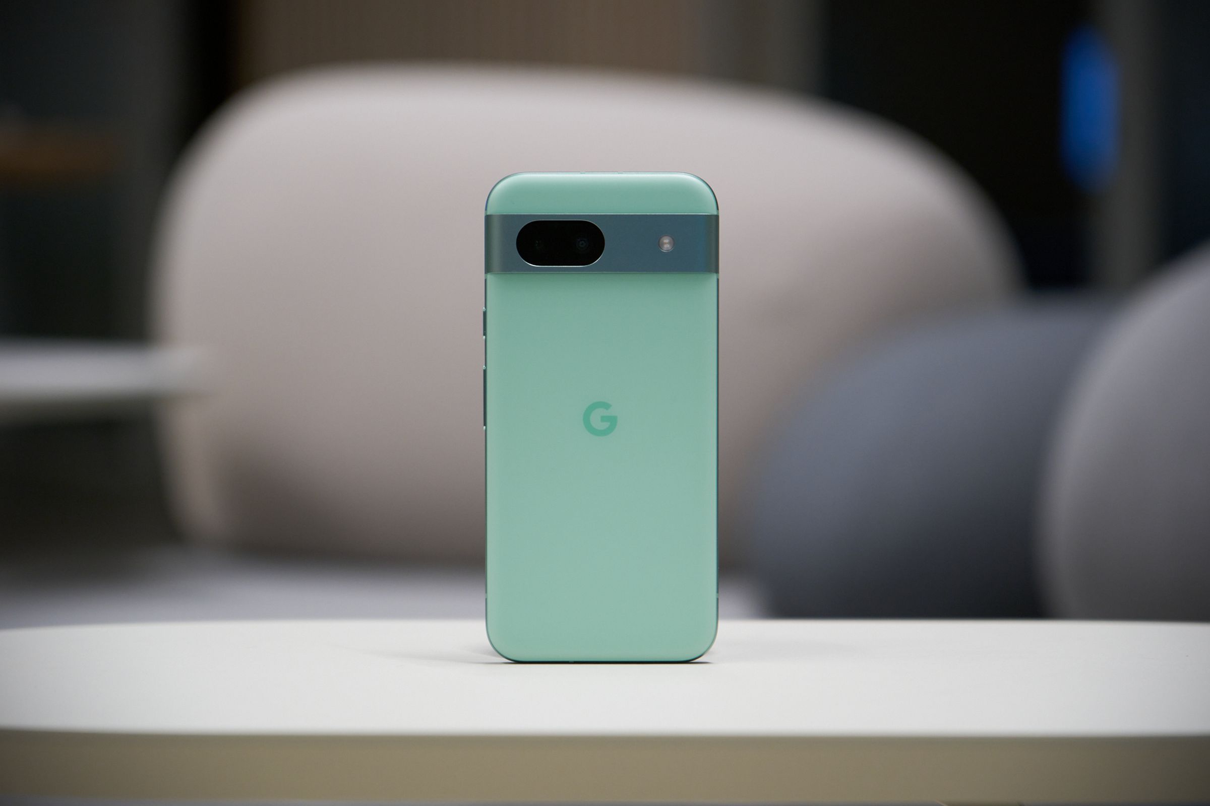 An image of an aloe-colored Google Pixel 8A placed upright in the center of a table.