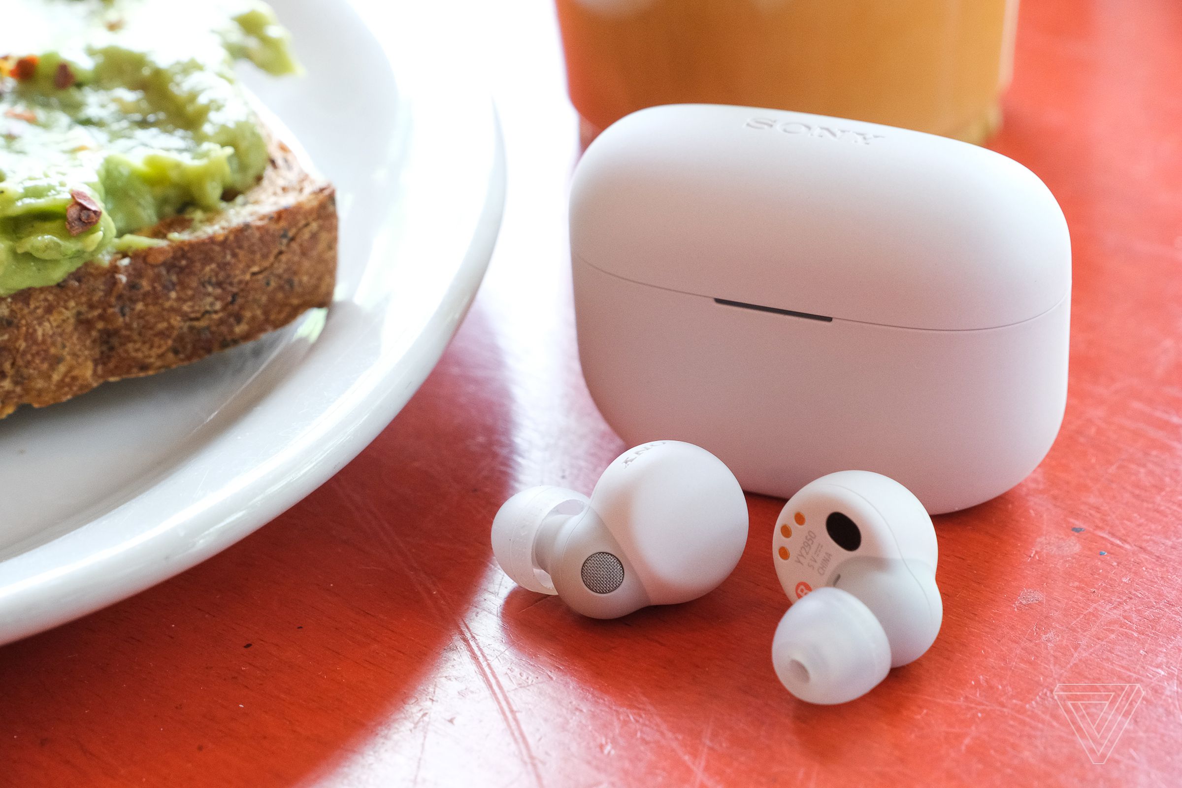 The white Sony LinkBuds S earbuds resting on a table outside their case, beside a plate of food.