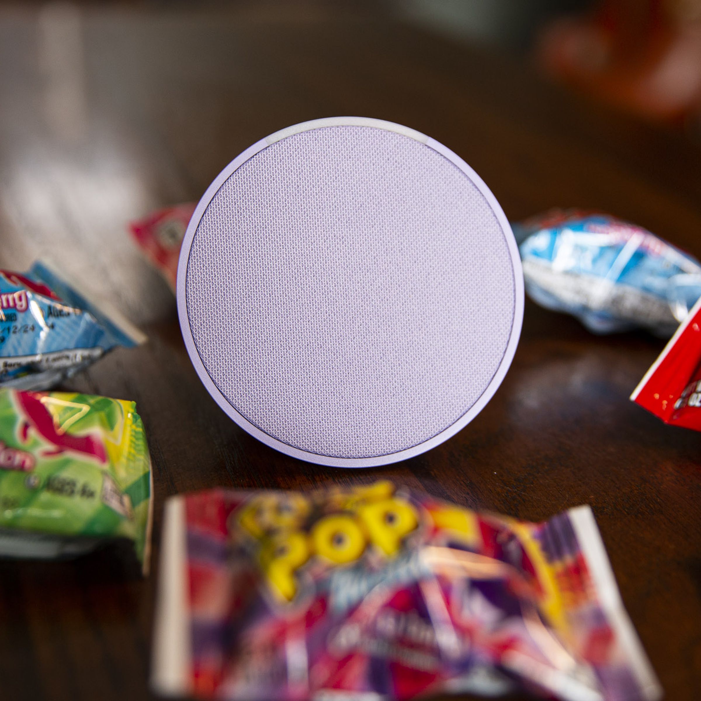A purple Echo Pop smart speaker on a table surrounded by Ring Pop candy.