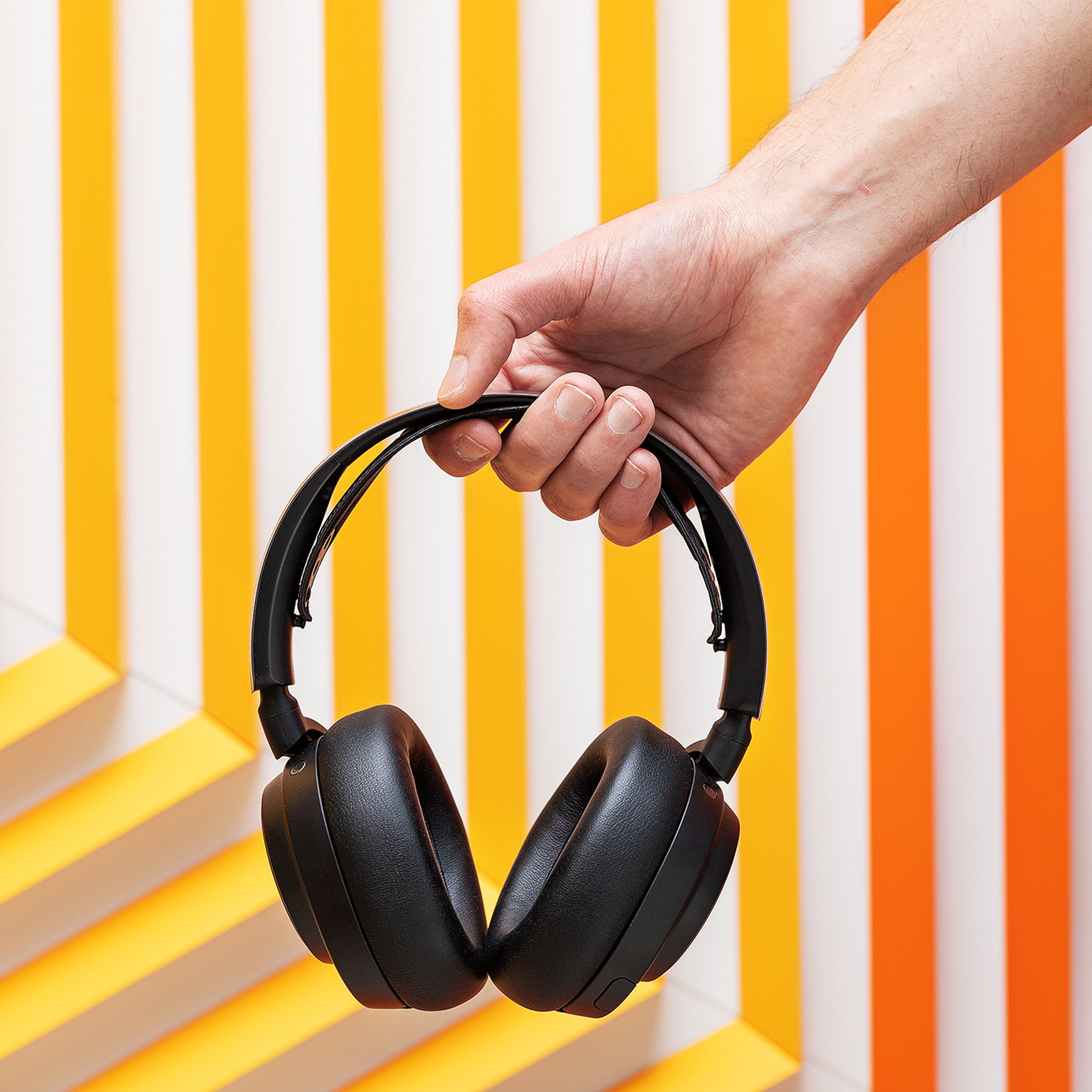 A picture of a hand holding up the black headset, on a background of orange and yellow stripes set in a geometric pattern.