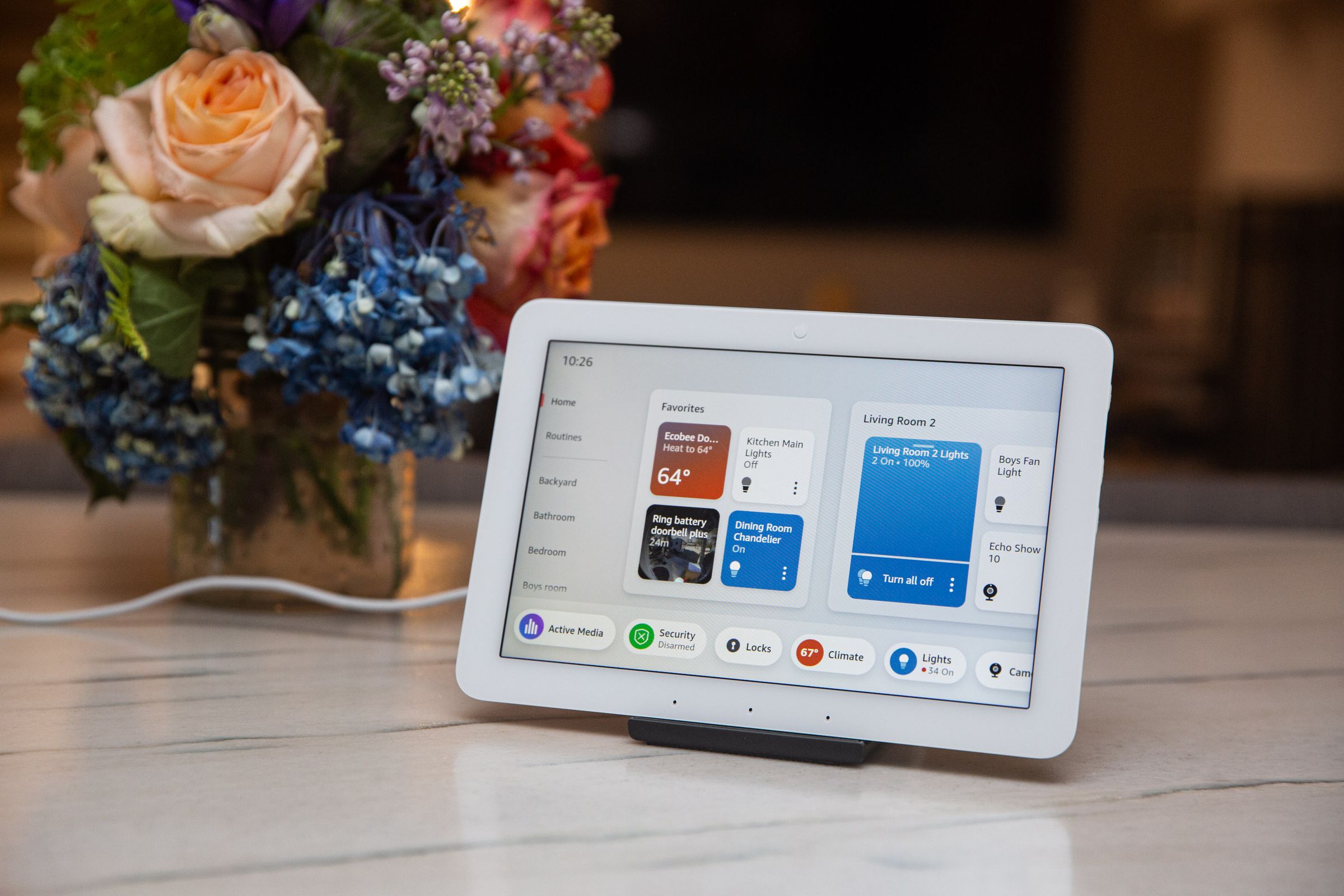 A small touchscreen tablet on a counter next to some flowers.