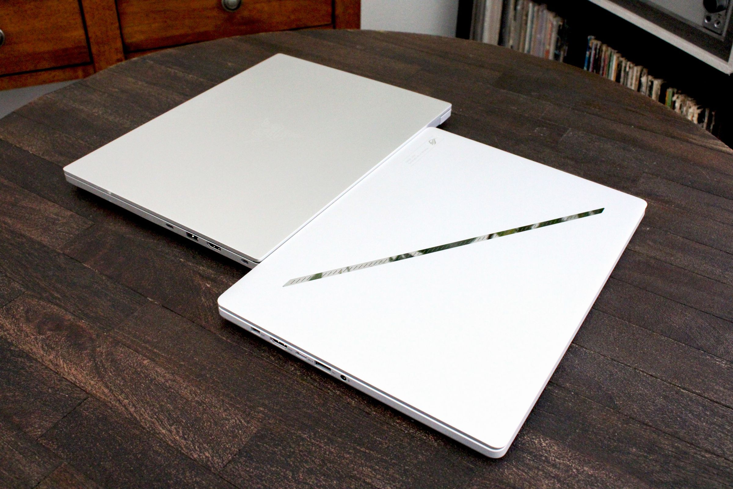 Two laptops with their lids closed next to one another on top of a dark wood table