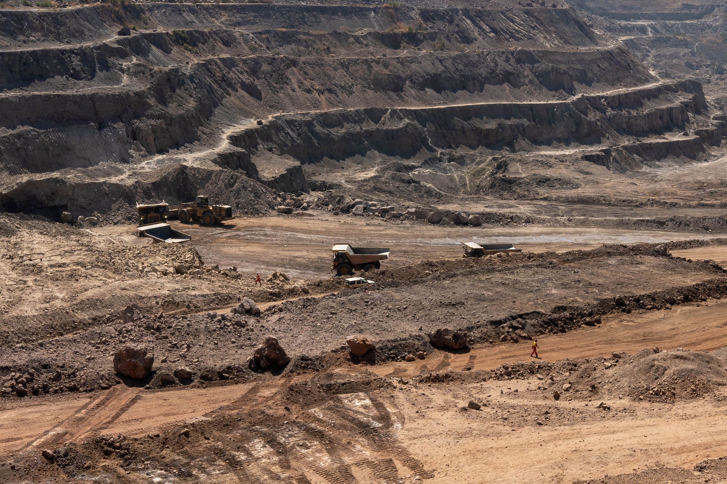 Trucks drive across an open-pit mine.