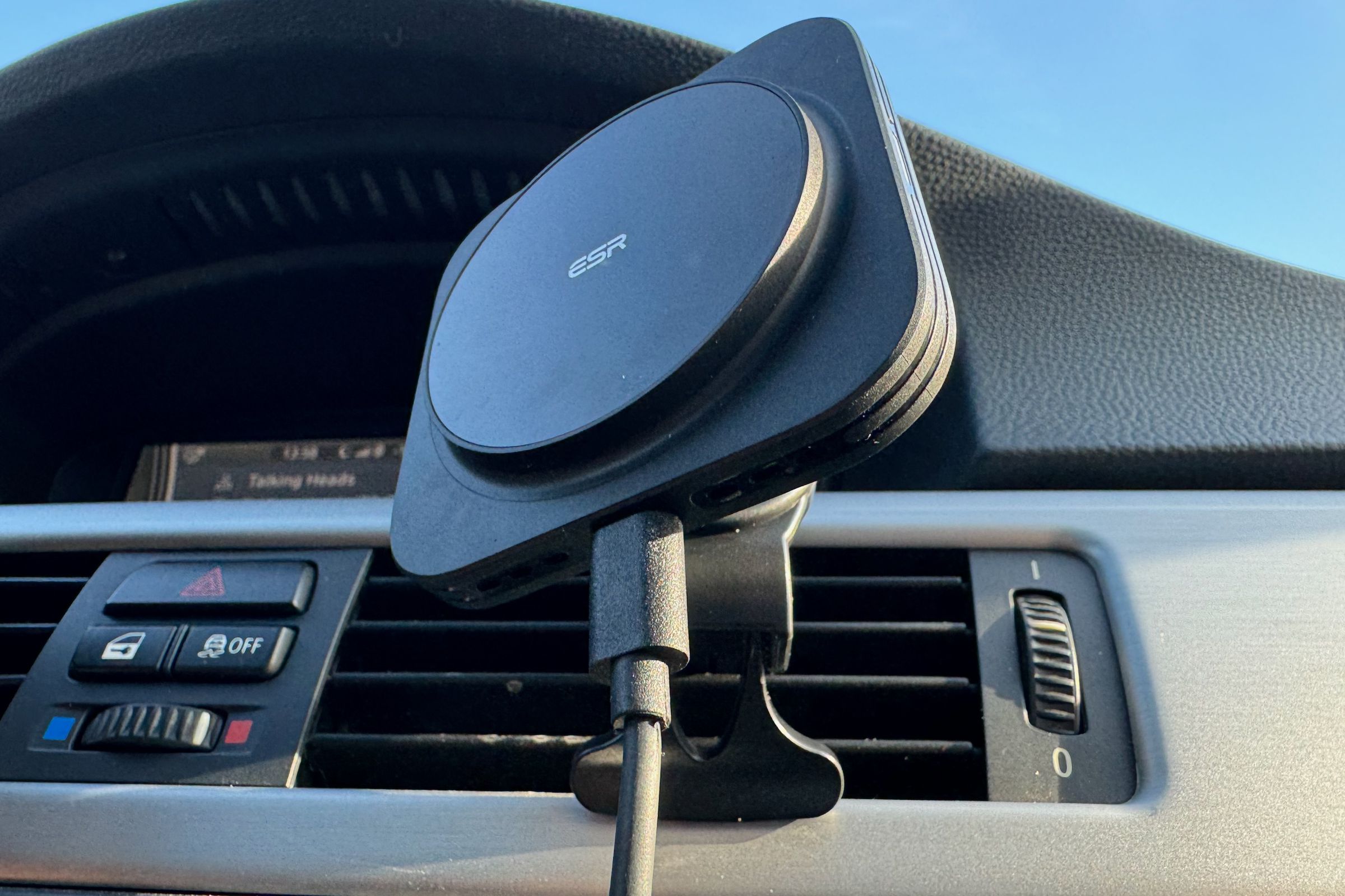 A black plastic car charging mount with the ESR logo at the center of the circular charging puck is mounted to a car’s vent.