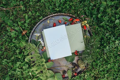 White empty sheet of paper on metallic misc with berries and flowers, white card mockup on natural b