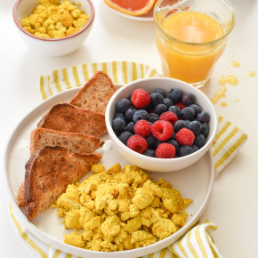 A breakfast table with a a plate of scrambled tofu eggs and a slice of toast with berries.