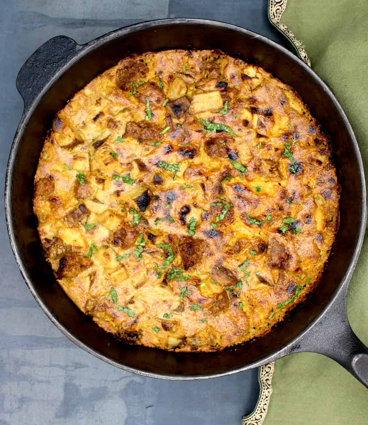 Vegan breakfast casserole baked in cast iron pan with a green napkin on the side.