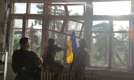 Soldiers waving a Ukrainian flag out of the window of a damaged building