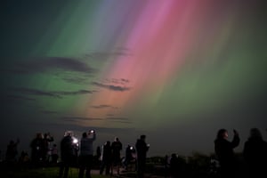People gather with phones to take a photo of the green and pink sky