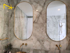 a bathroom with marble walls and two oval mirrors on the wall next to each other